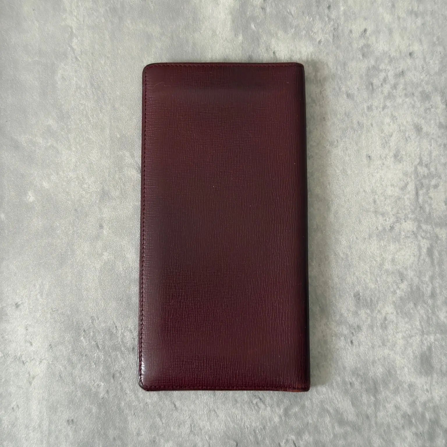Cartier Must de Cartier Bifold Long Wallet in rich burgundy leather, detailed with multiple card slots, bill compartments, and a discreet embossed logo on the front cover.