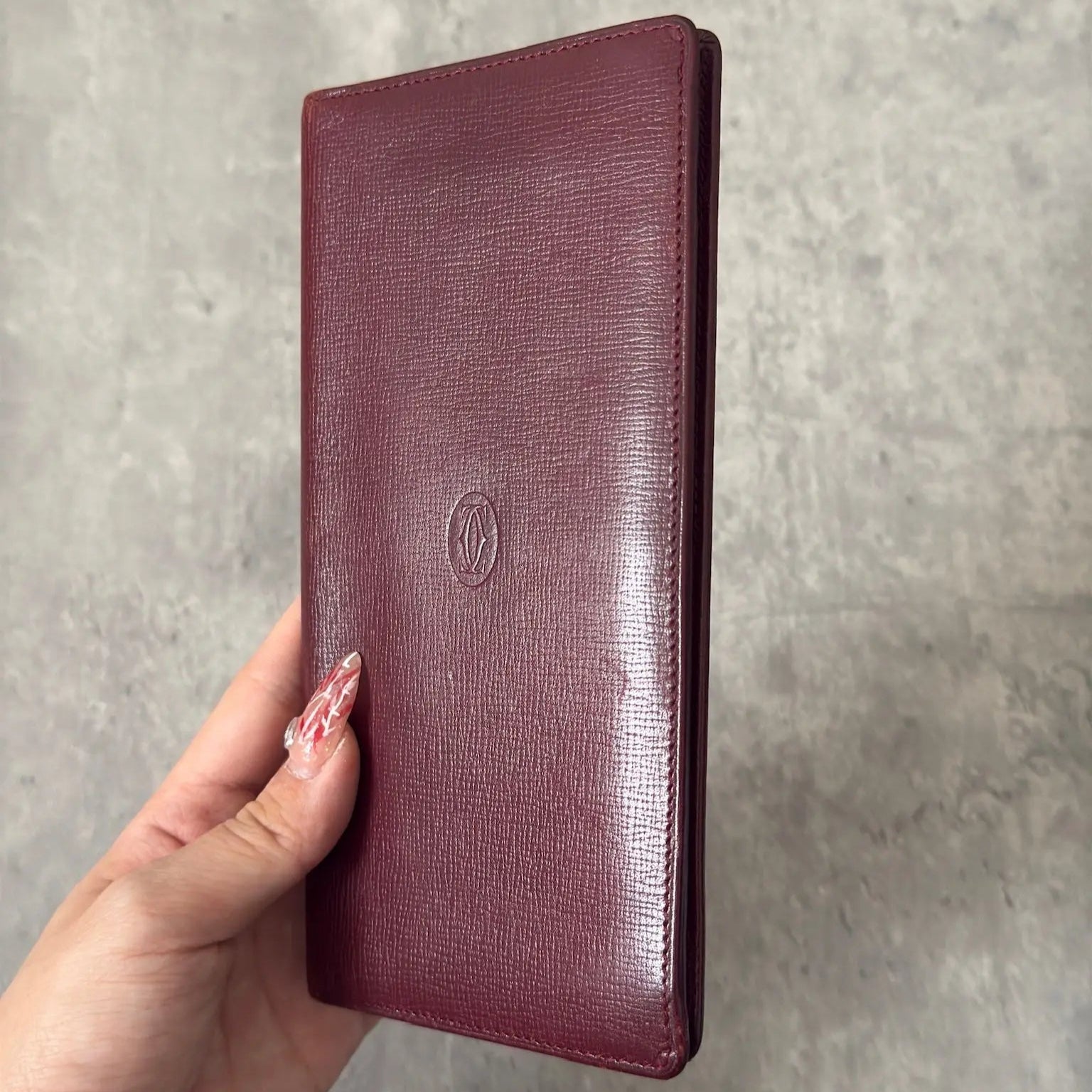 Cartier Must de Cartier Bifold Long Wallet in rich burgundy leather, detailed with multiple card slots, bill compartments, and a discreet embossed logo on the front cover.