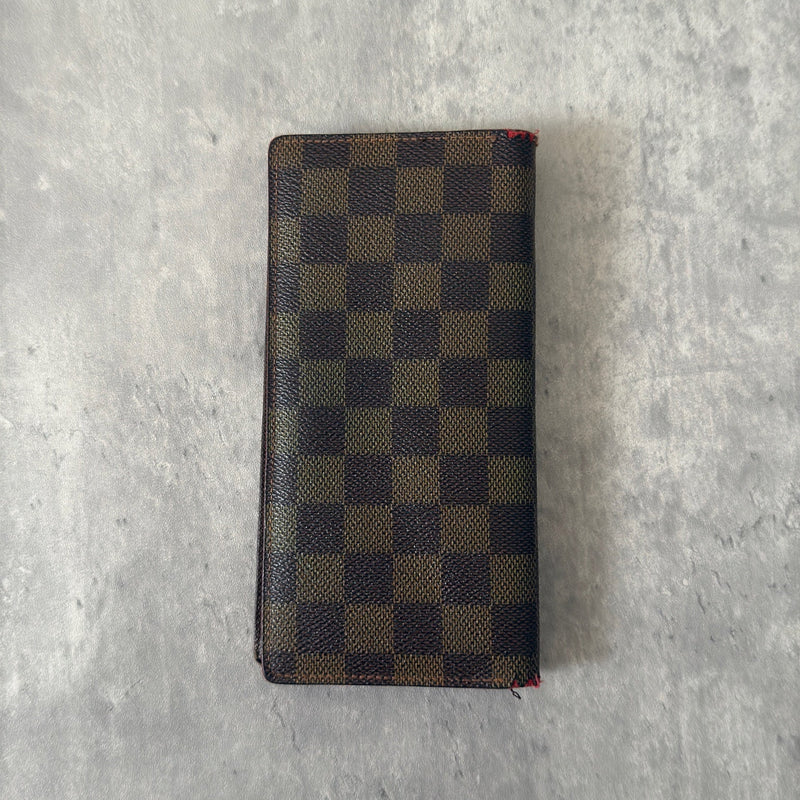 Louis Vuitton Damier Ebene Brazza wallet in dark brown and black checkered canvas, featuring a snap closure and organized interior with card slots and bill compartments.