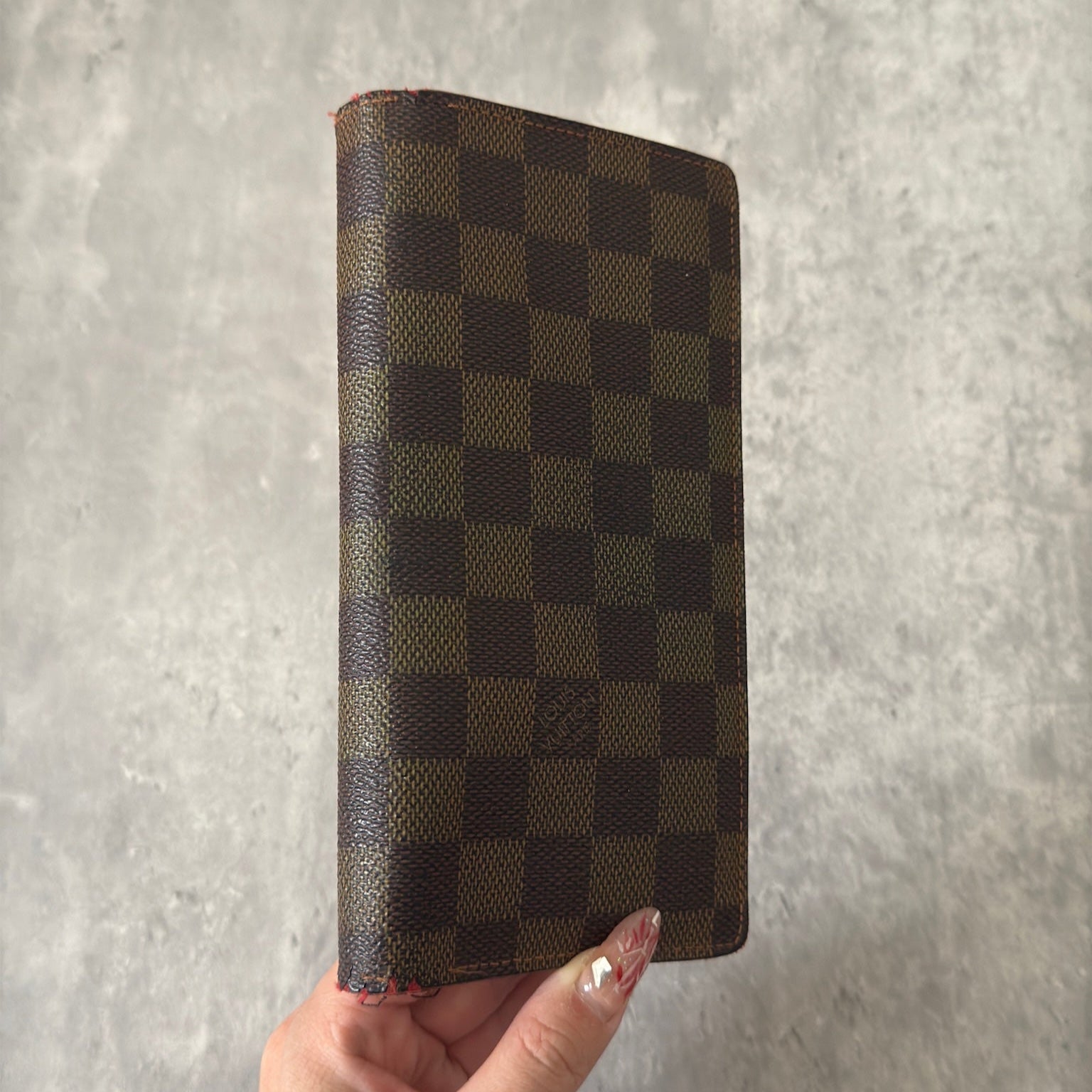 Louis Vuitton Damier Ebene Brazza wallet in dark brown and black checkered canvas, featuring a snap closure and organized interior with card slots and bill compartments.