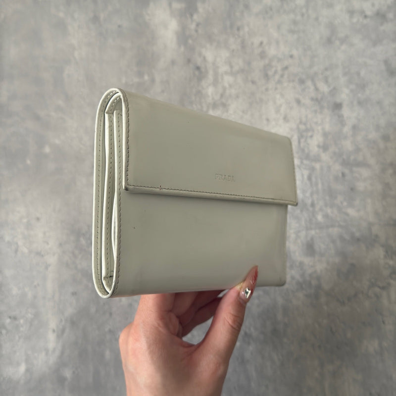 Prada City Calf Leather Compact Wallet in off-white with flap closure and embossed logo detail, showcasing a sophisticated, minimalist design.