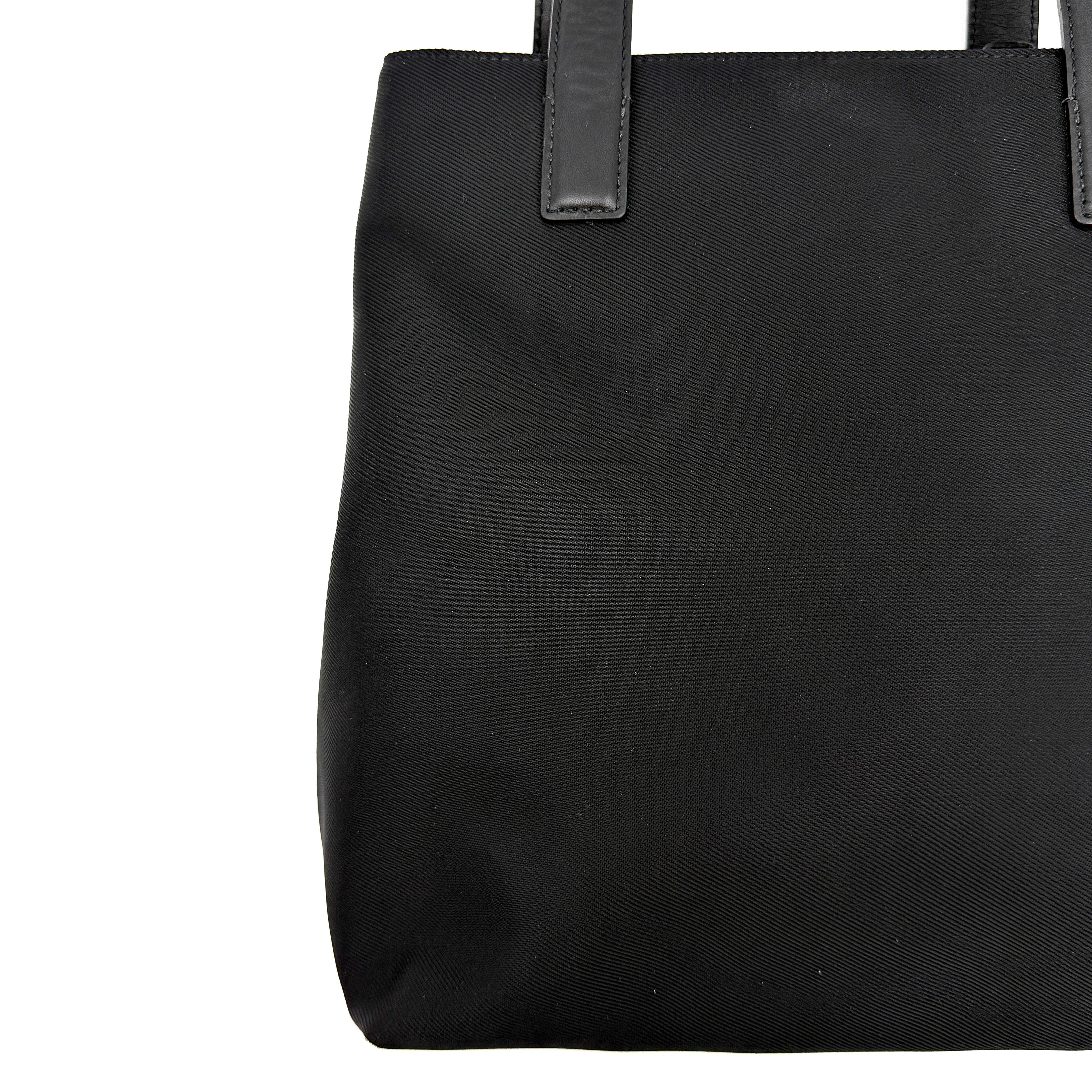 Coach Mercer Nylon Tote Bag in black with structured silhouette, leather handles, and subtle silver logo plaque at the base.