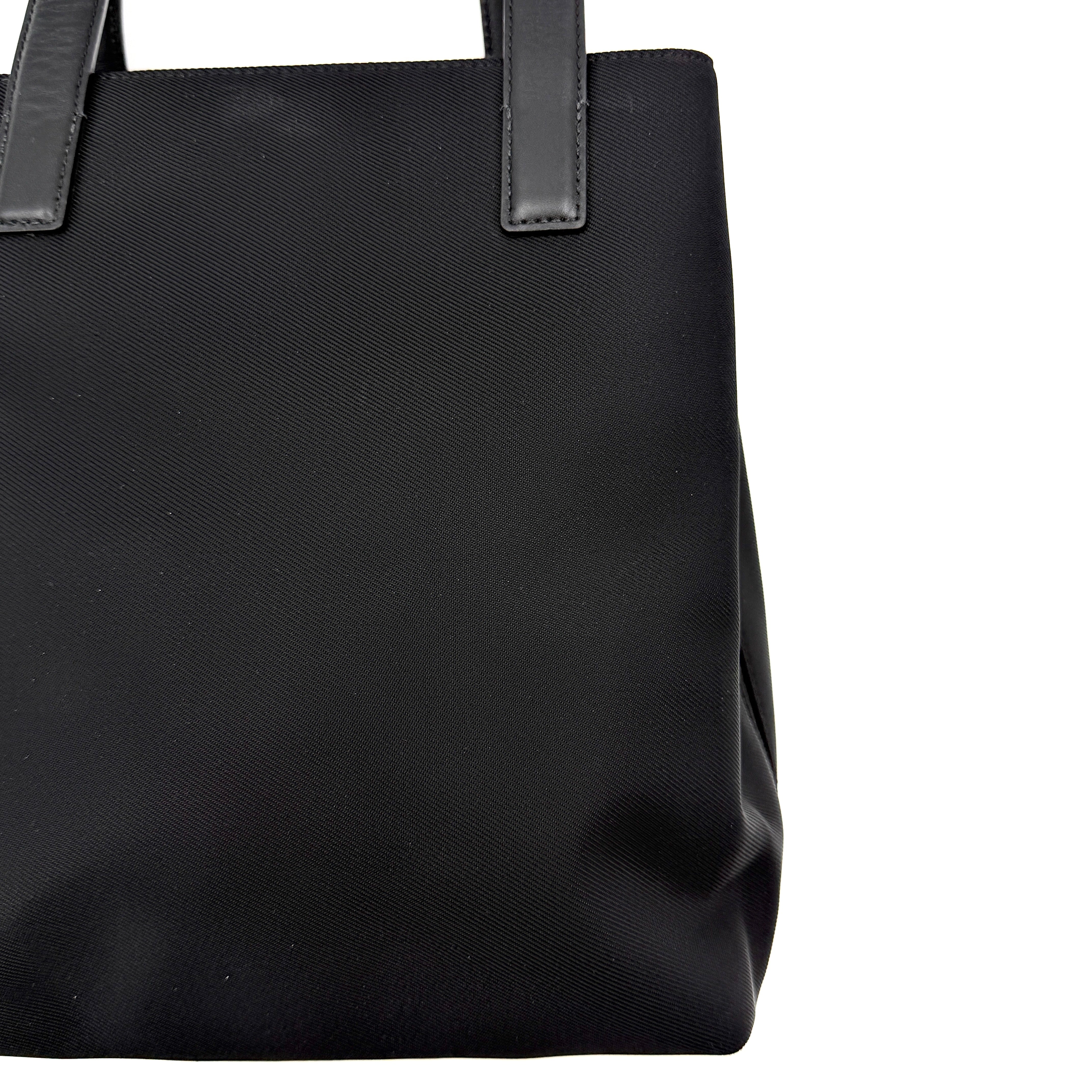 Coach Mercer Nylon Tote Bag in black with structured silhouette, leather handles, and subtle silver logo plaque at the base.