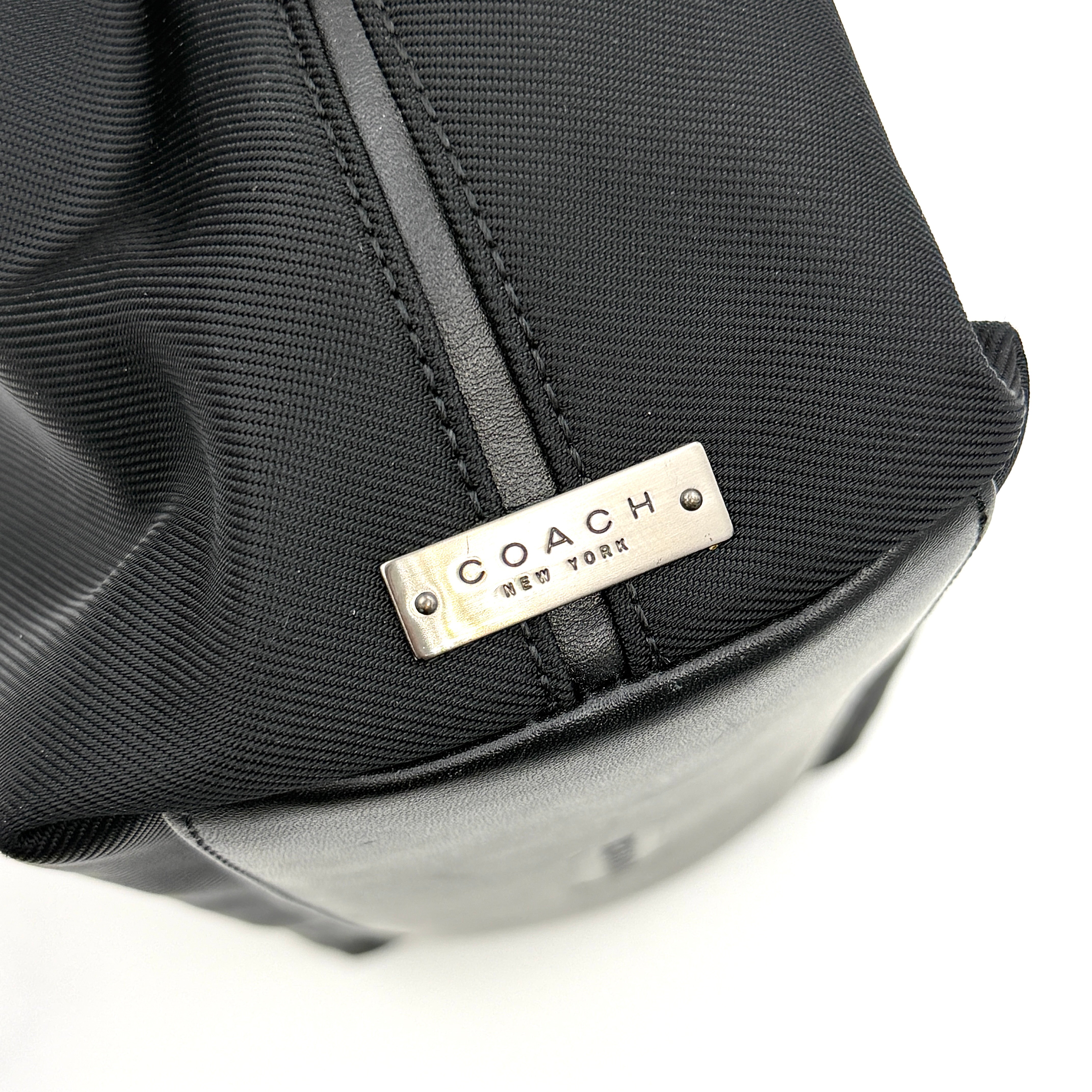 Coach Mercer Nylon Tote Bag in black with structured silhouette, leather handles, and subtle silver logo plaque at the base.
