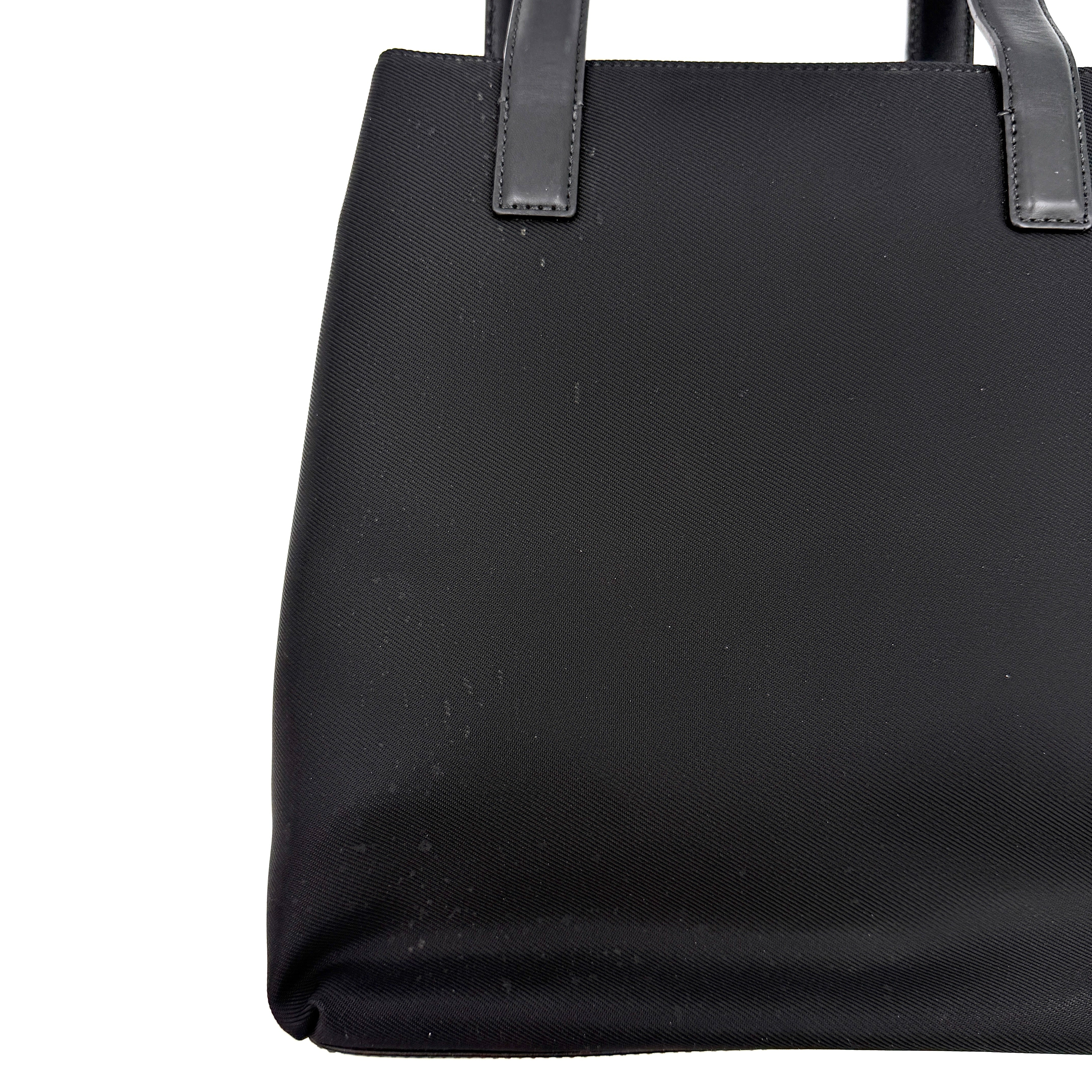 Coach Mercer Nylon Tote Bag in black with structured silhouette, leather handles, and subtle silver logo plaque at the base.