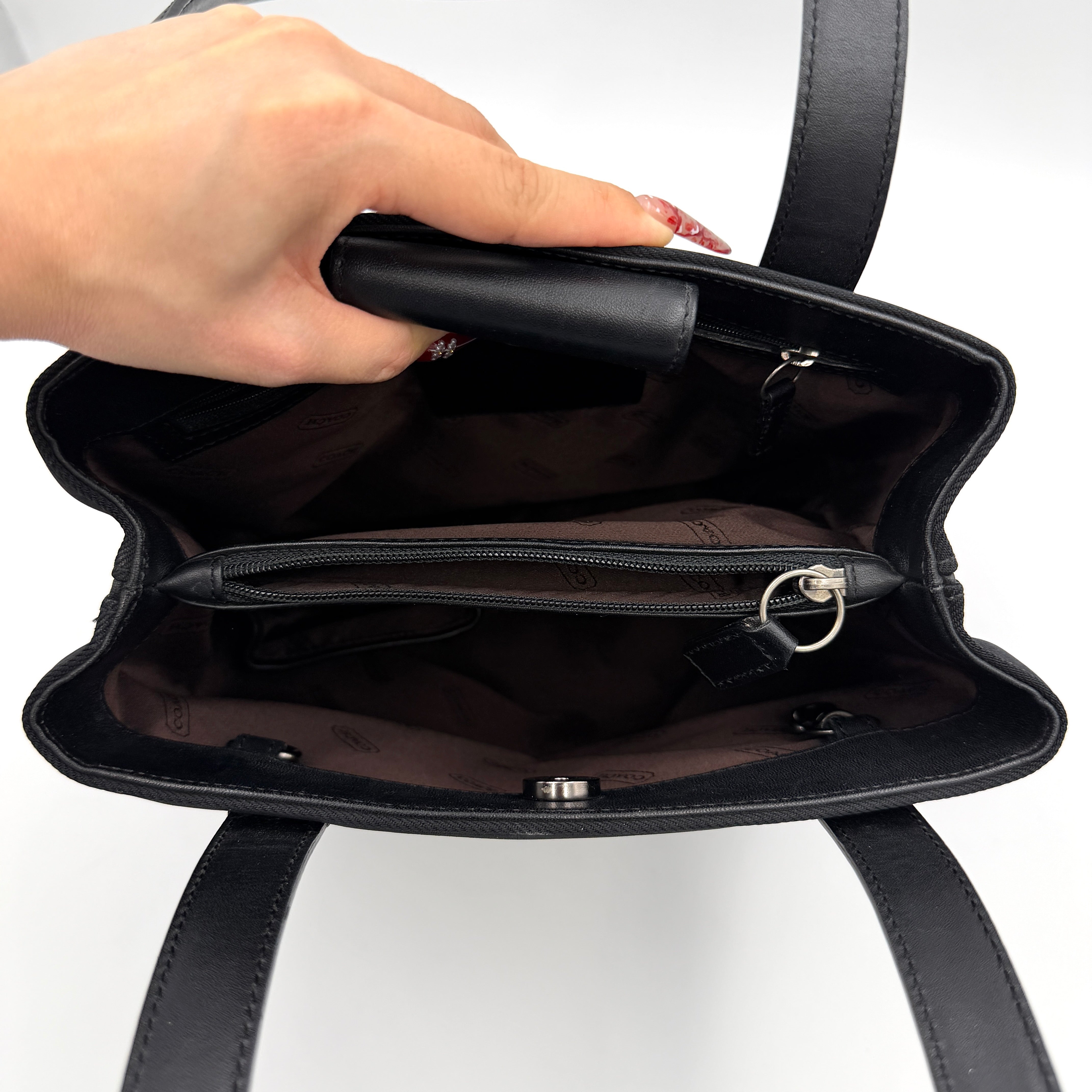 Coach Mercer Nylon Tote Bag in black with structured silhouette, leather handles, and subtle silver logo plaque at the base.