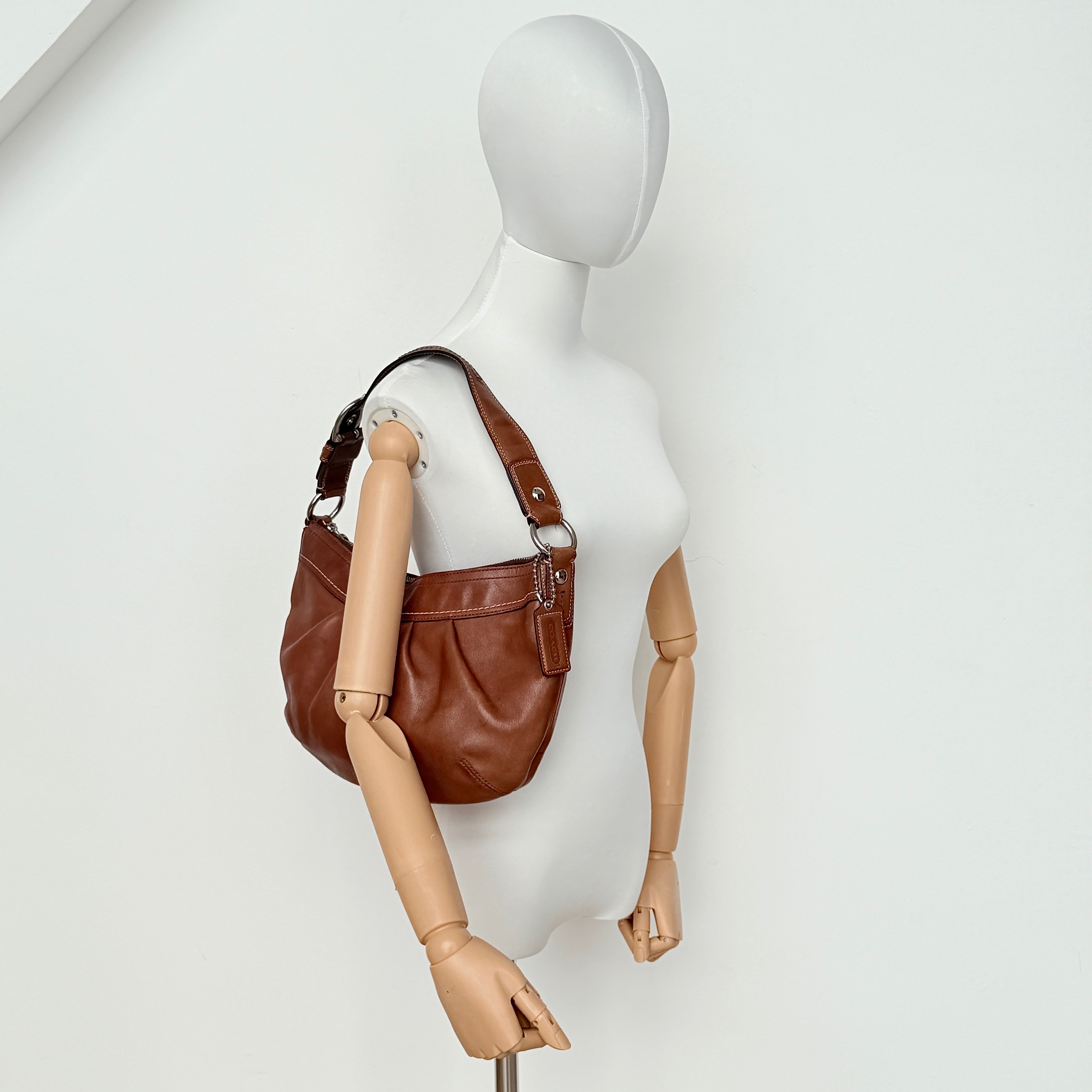 Coach Soho Hobo brown leather shoulder bag with pleated detailing and silver hardware, shown on a white background.