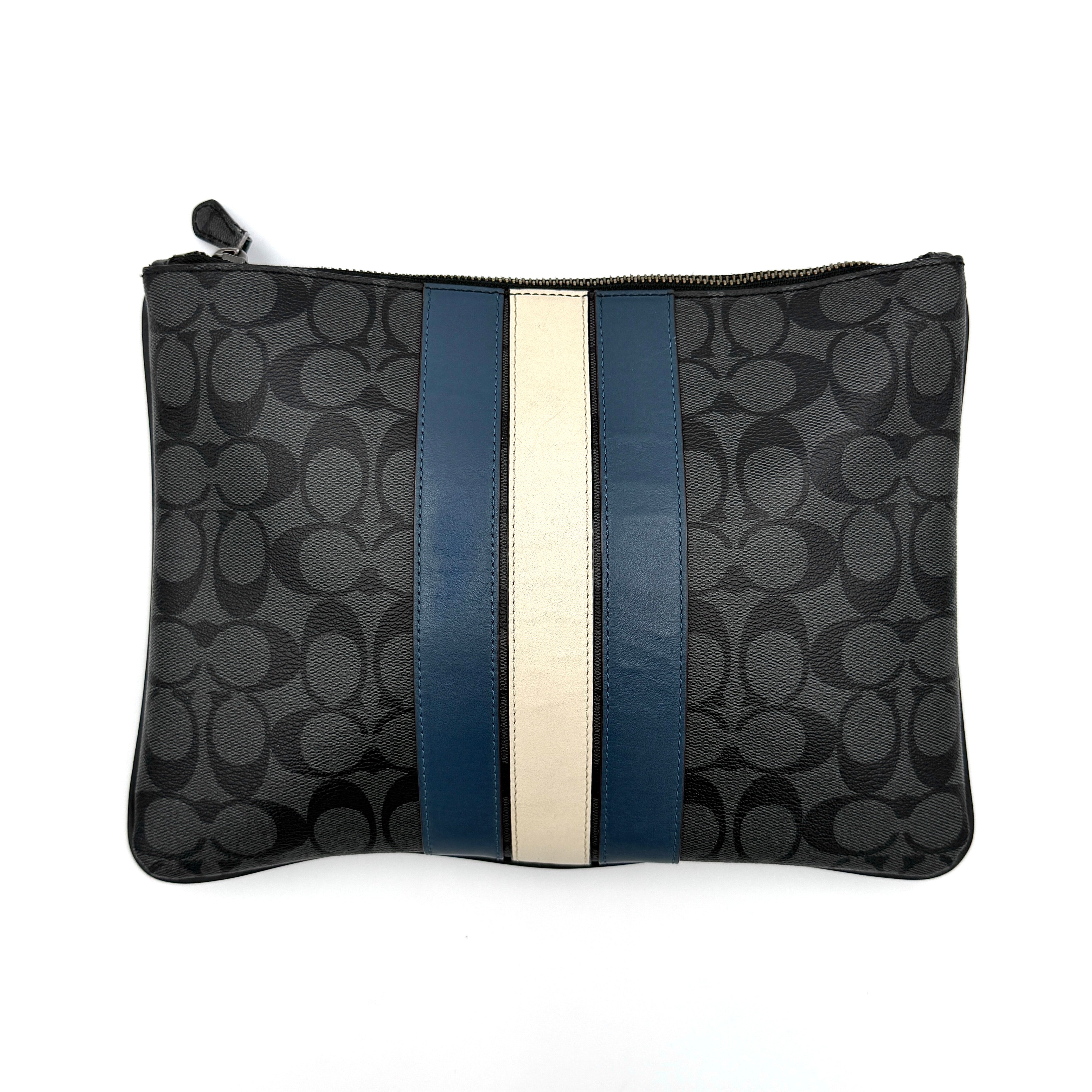 Coach Signature large pouch in black coated canvas with navy and cream varsity stripes, shown from the front with a zip top.