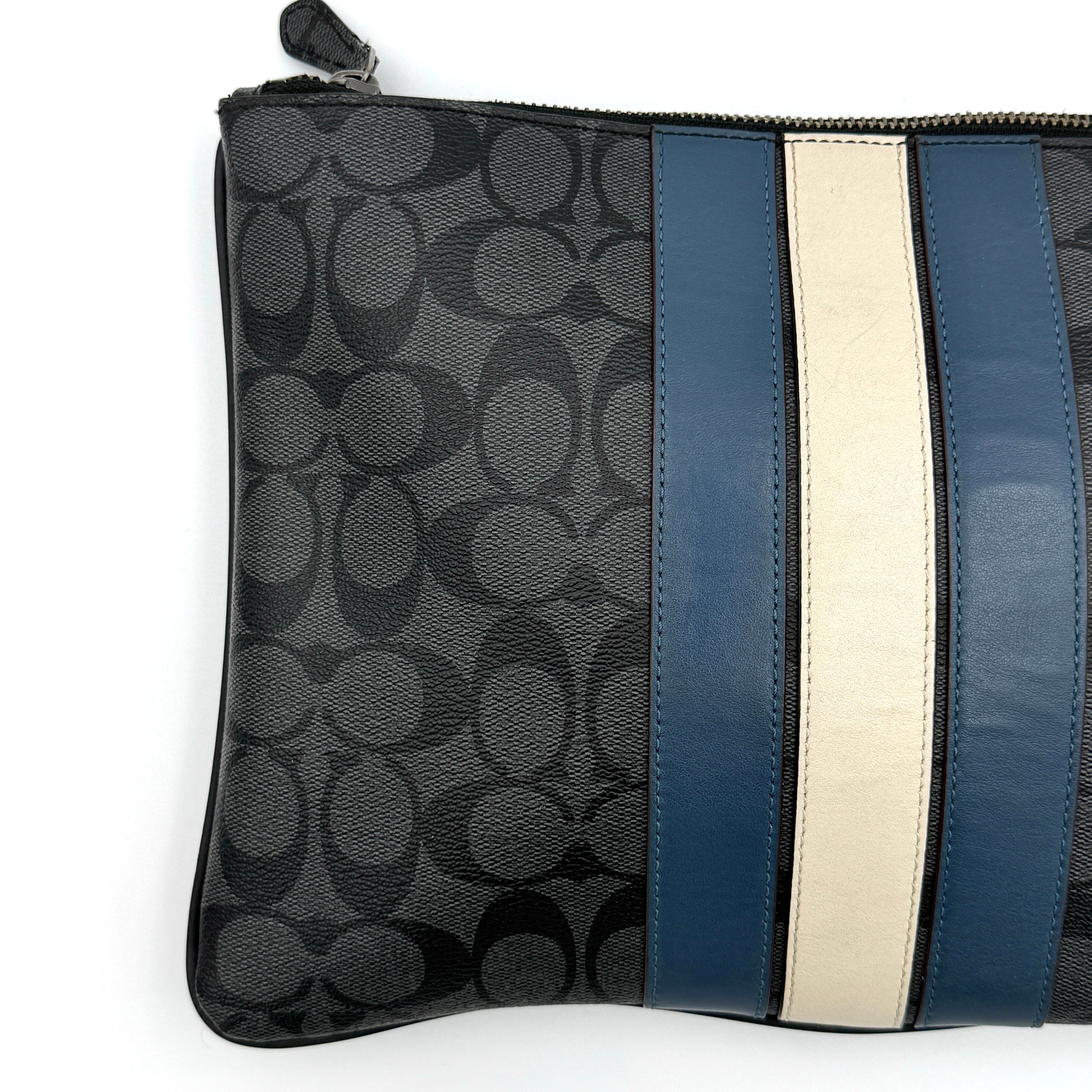 Coach Signature large pouch in black coated canvas with navy and cream varsity stripes, shown from the front with a zip top.