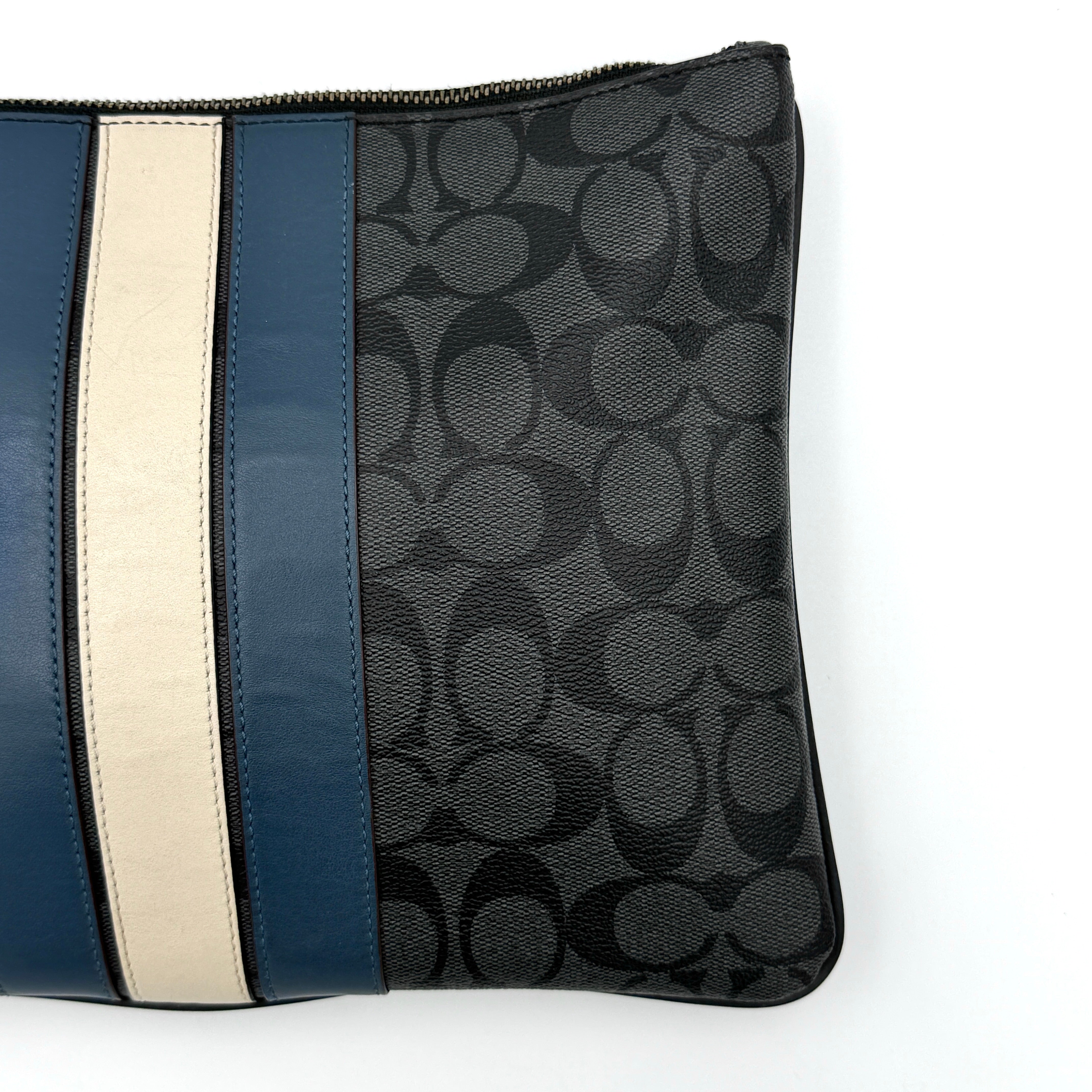 Coach Signature large pouch in black coated canvas with navy and cream varsity stripes, shown from the front with a zip top.