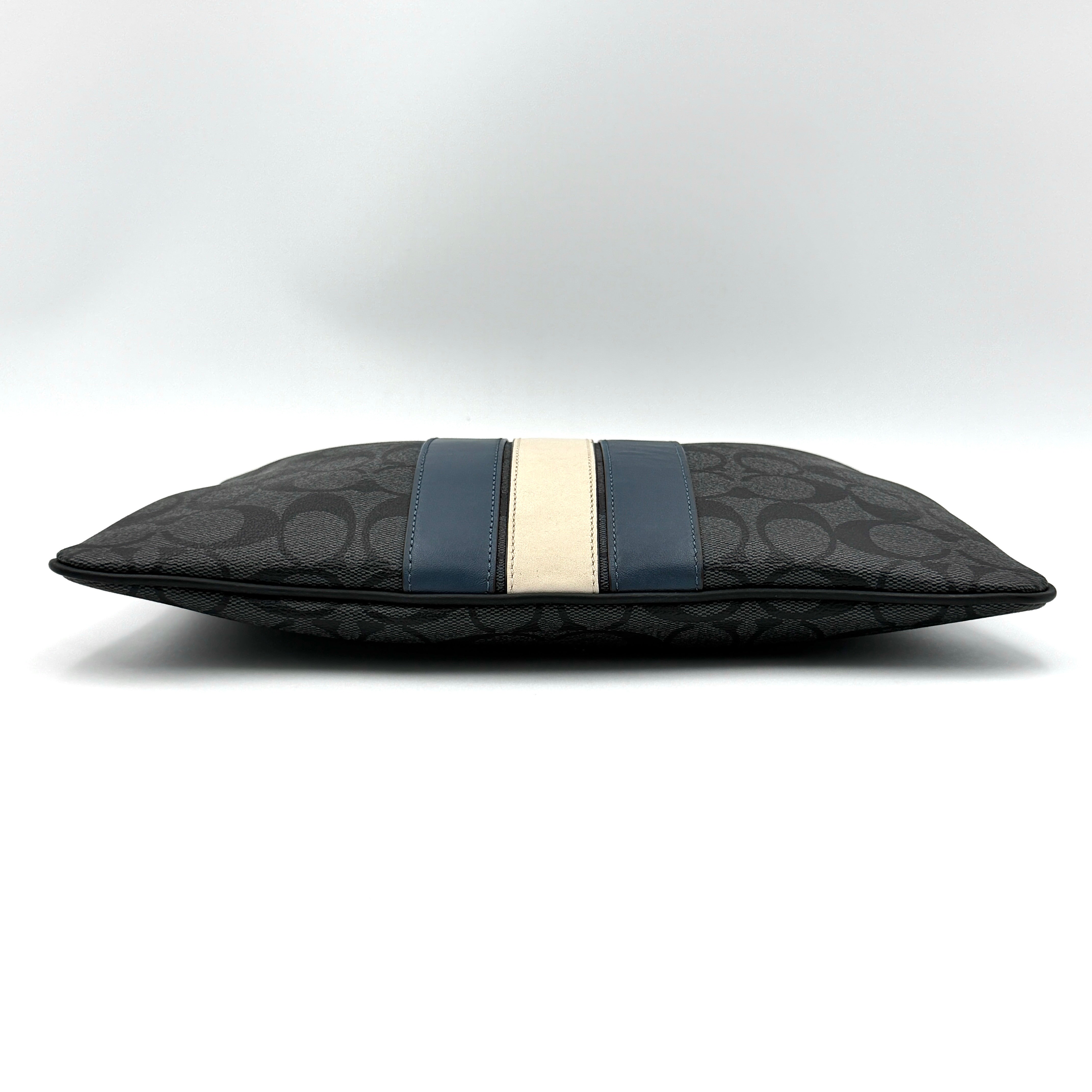 Coach Signature large pouch in black coated canvas with navy and cream varsity stripes, shown from the front with a zip top.