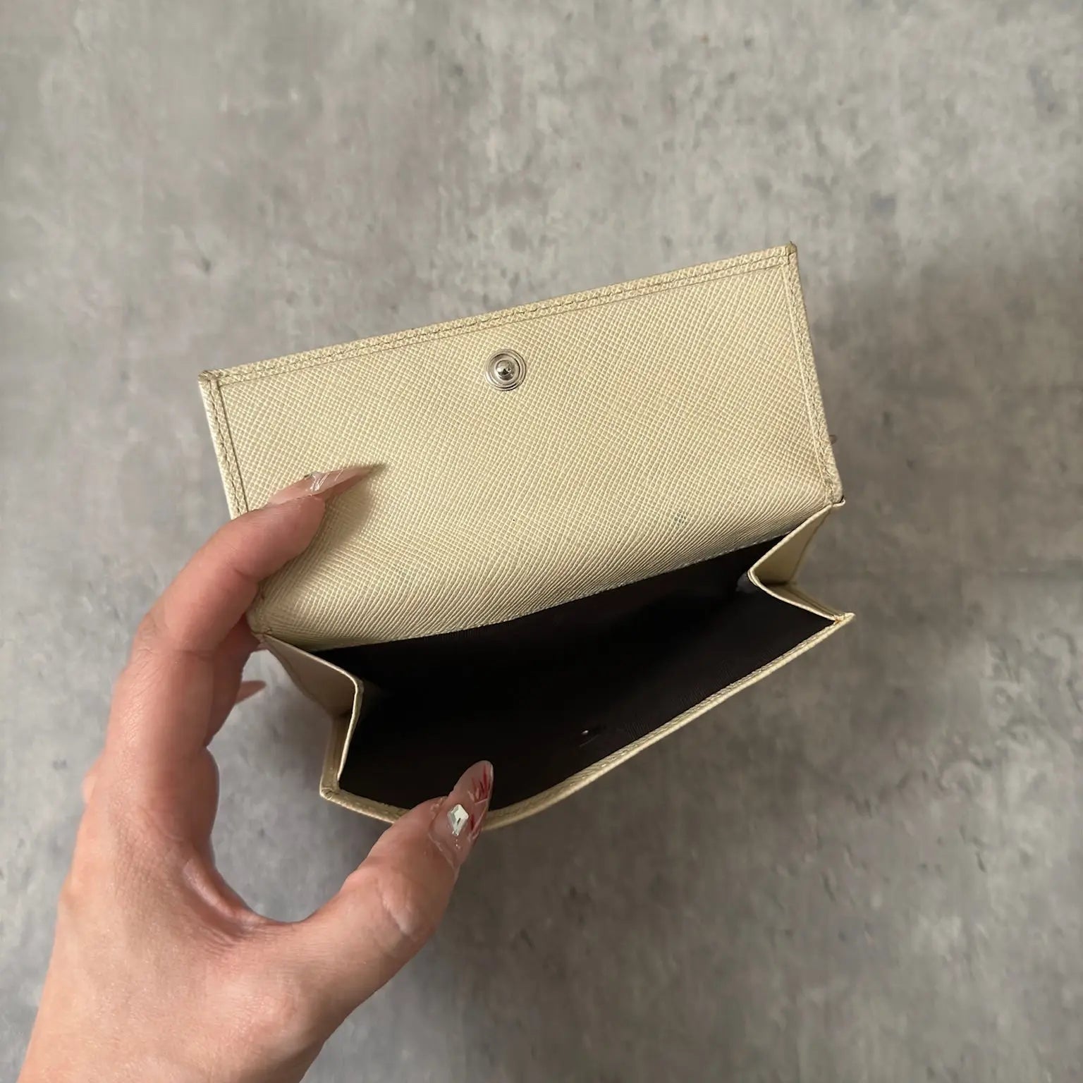 Prada Cream Saffiano Folding Leather Wallet, crafted from textured Saffiano leather with a gold-tone triangular logo and a compact folding design.