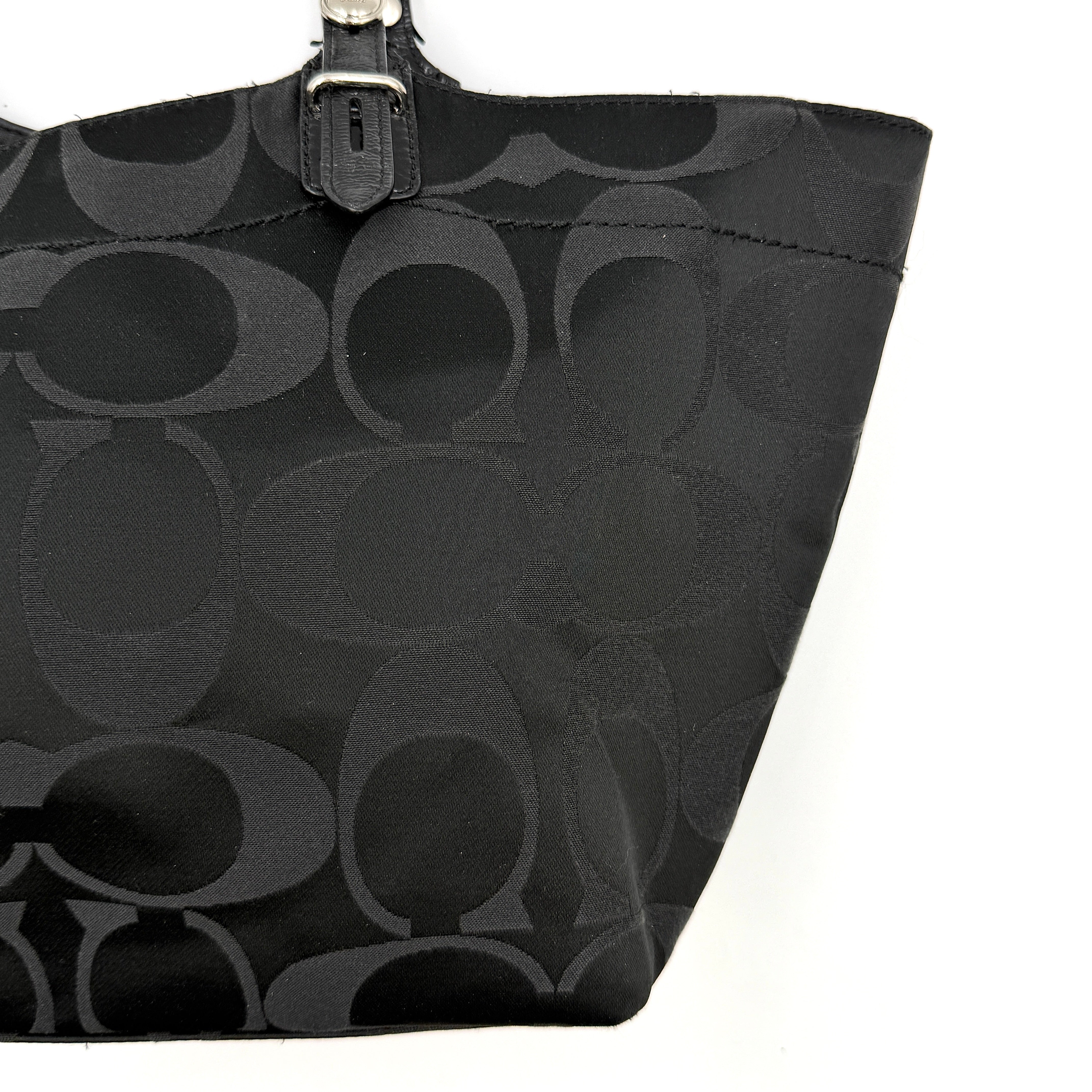 Coach black signature canvas tote with leather handles and silver hardware, set against a white background.