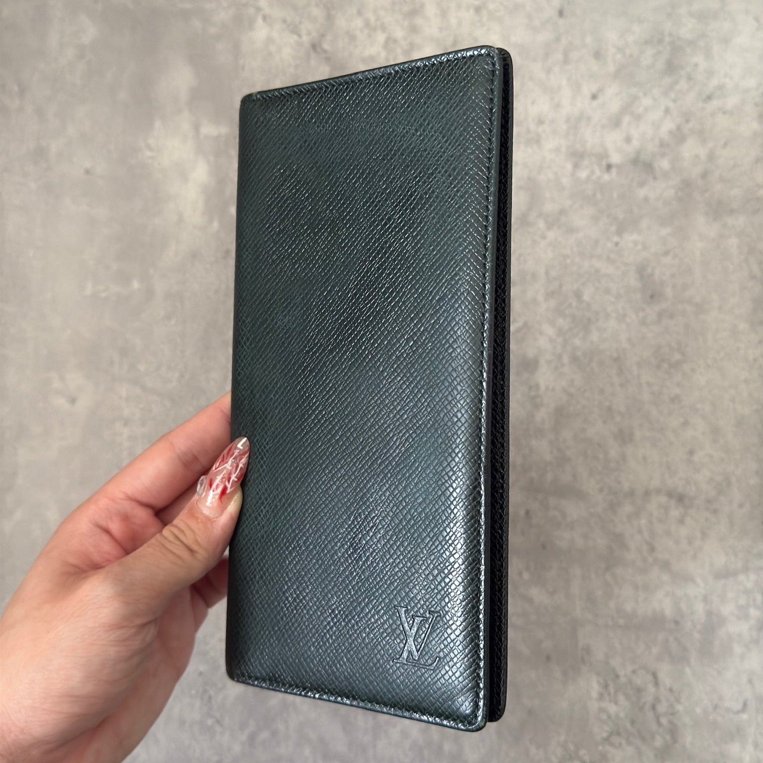 Louis Vuitton Taiga Porte-Valeurs long wallet in green, showcasing the embossed LV logo and a structured interior with multiple card slots and compartments, embodying luxury and organization.