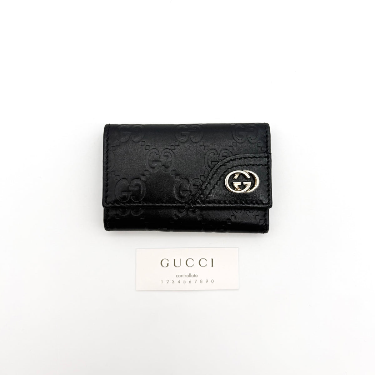Gucci black Guccissima monogram leather key case with silver-tone GG hardware and snap closure, presented on a white background.