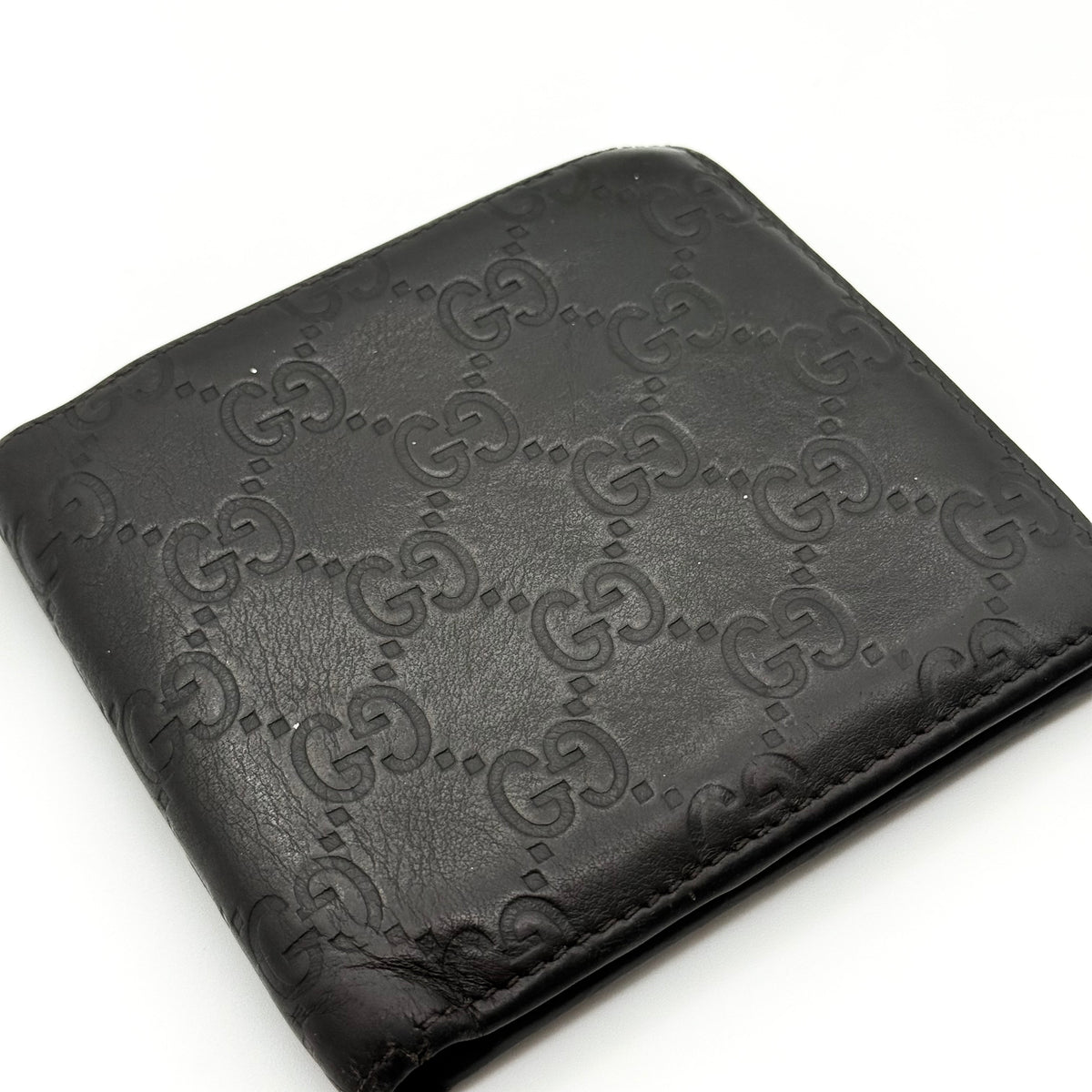 Gucci GG Guccissima bifold wallet in black leather with embossed monogram pattern, shown closed against a white background.