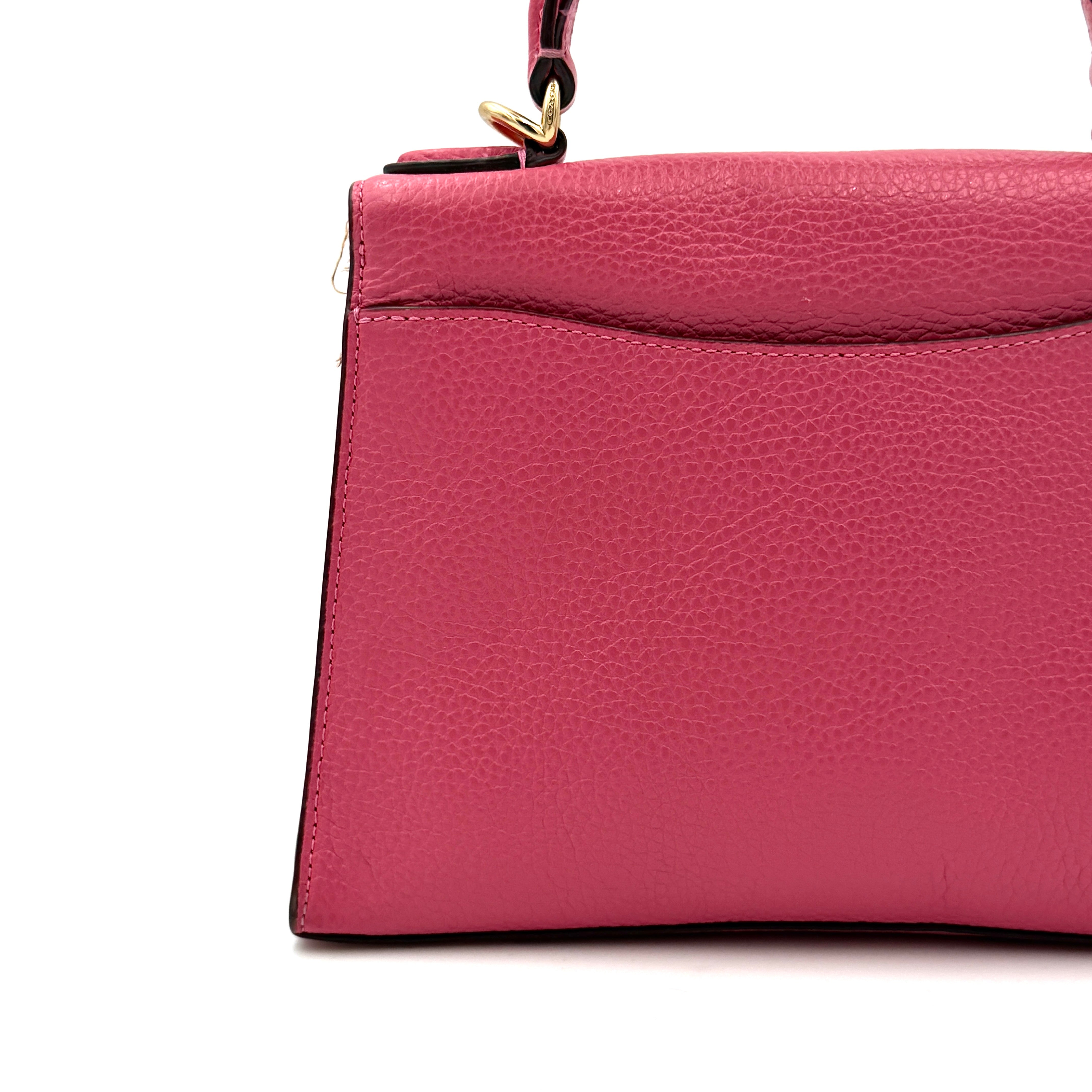 Coach Pepper Satchel in bold pink pebbled leather, featuring a structured silhouette and gold logo push-lock hardware.