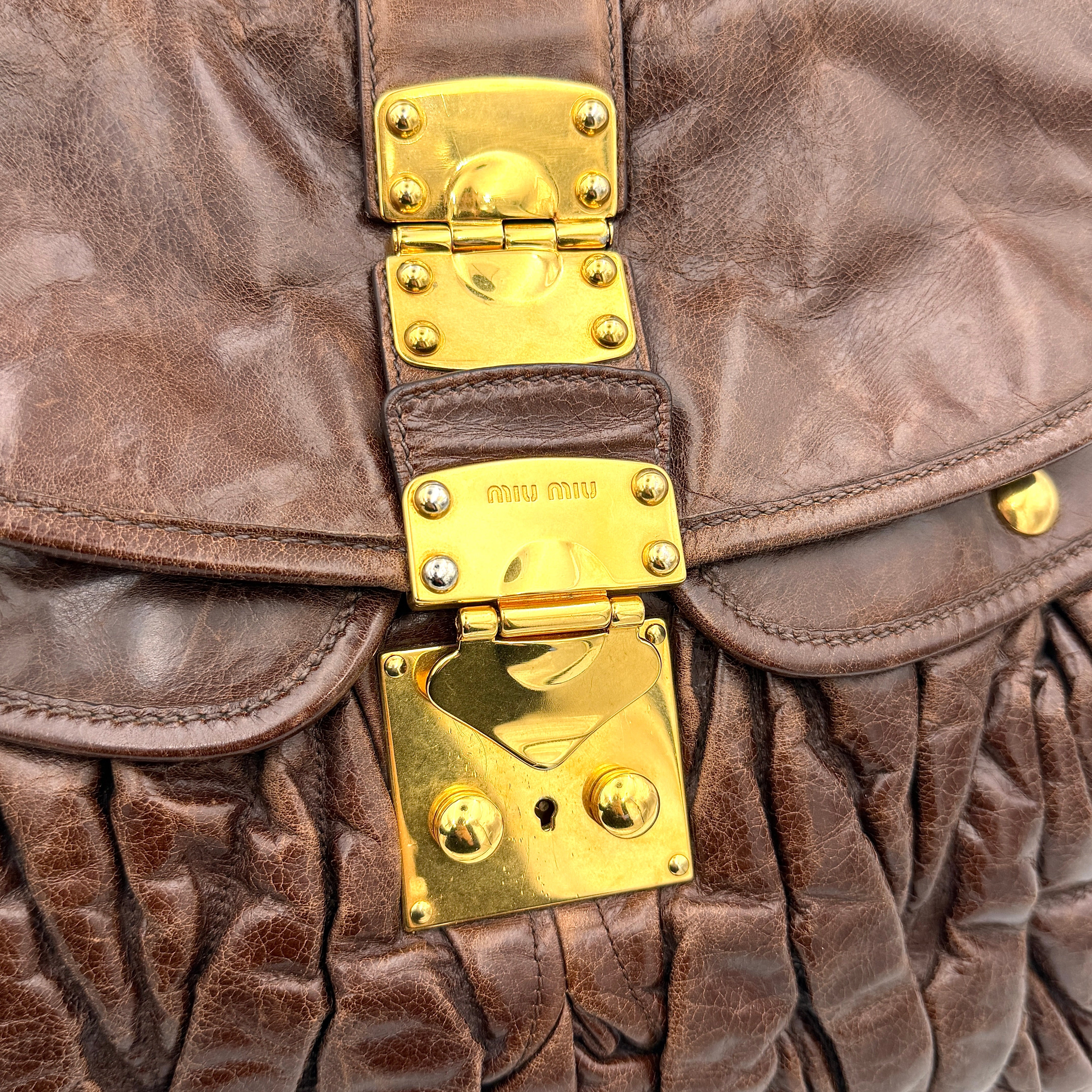 Miu Miu Coffer Hobo bag in deep brown matelassé leather with braided handle, gold hardware, and detachable strap.