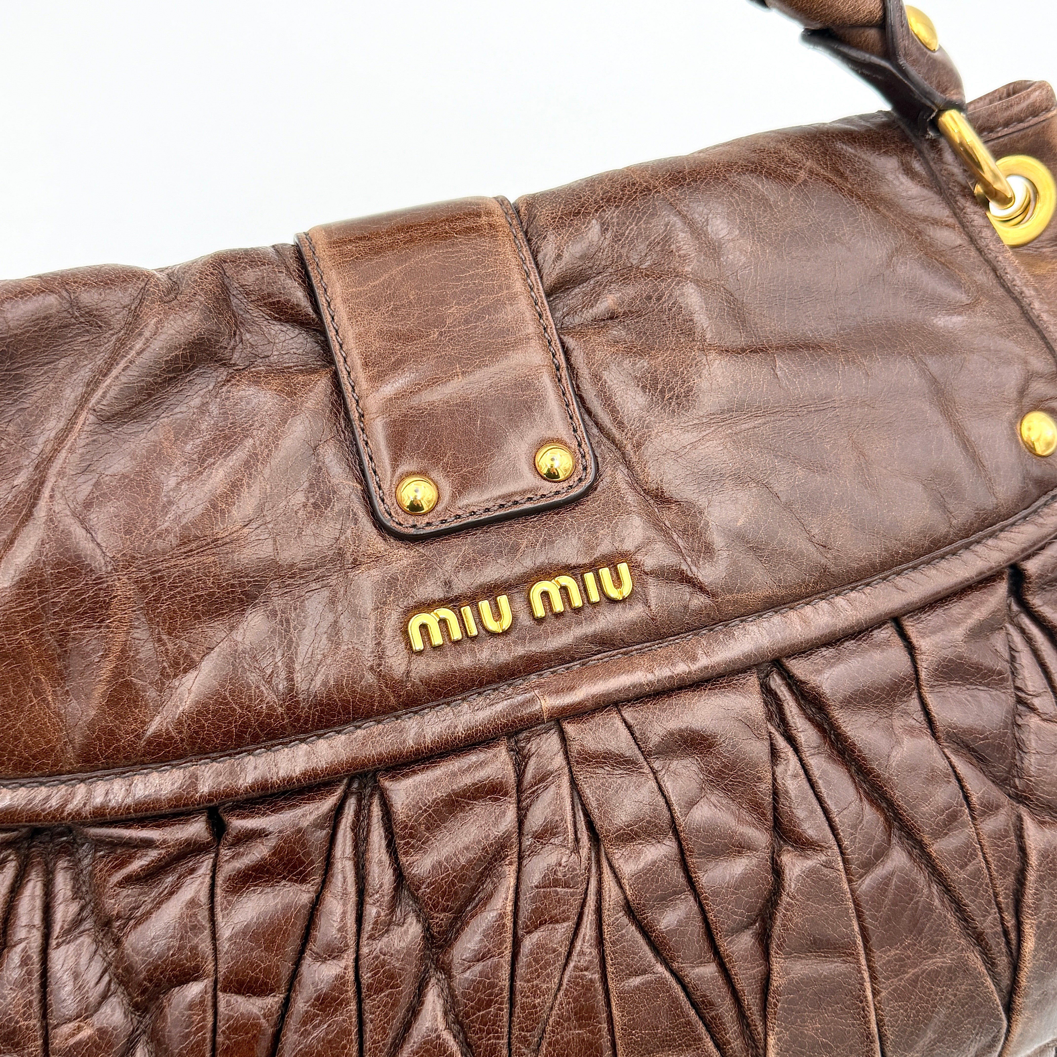 Miu Miu Coffer Hobo bag in deep brown matelassé leather with braided handle, gold hardware, and detachable strap.