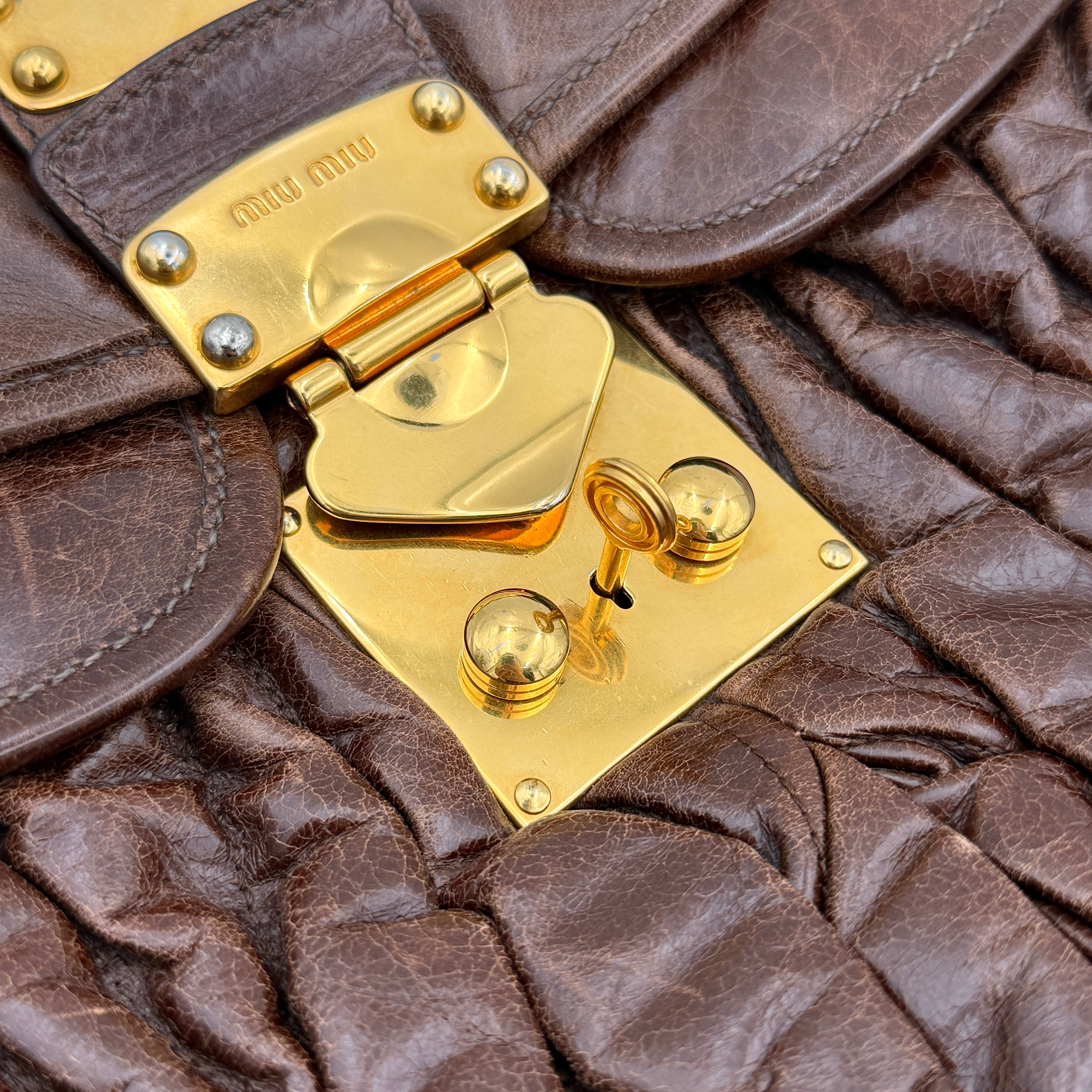 Miu Miu Coffer Hobo bag in deep brown matelassé leather with braided handle, gold hardware, and detachable strap.