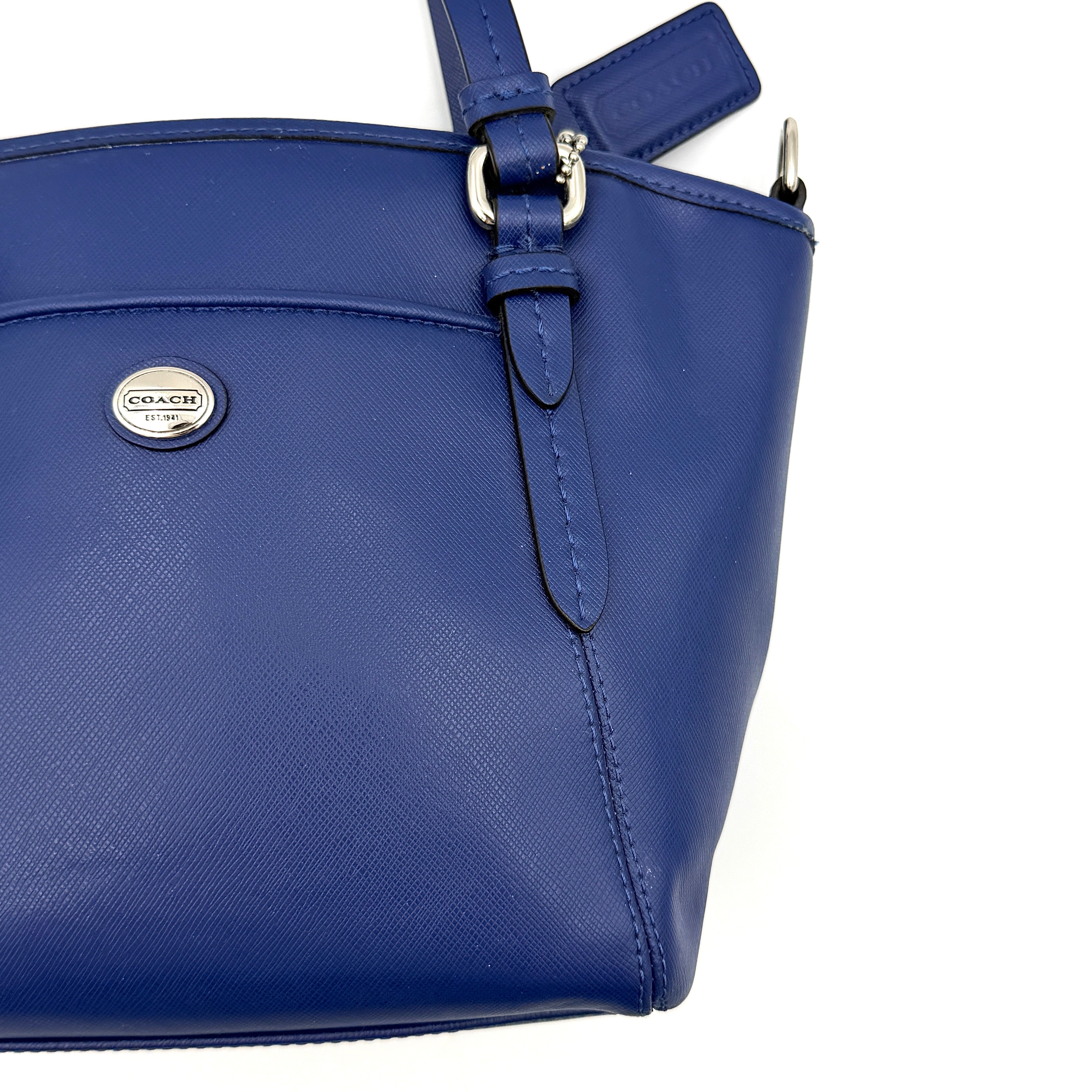 A structured cobalt blue Coach tote bag with silver hardware, dual handles, and an optional crossbody strap, displayed against a clean background.