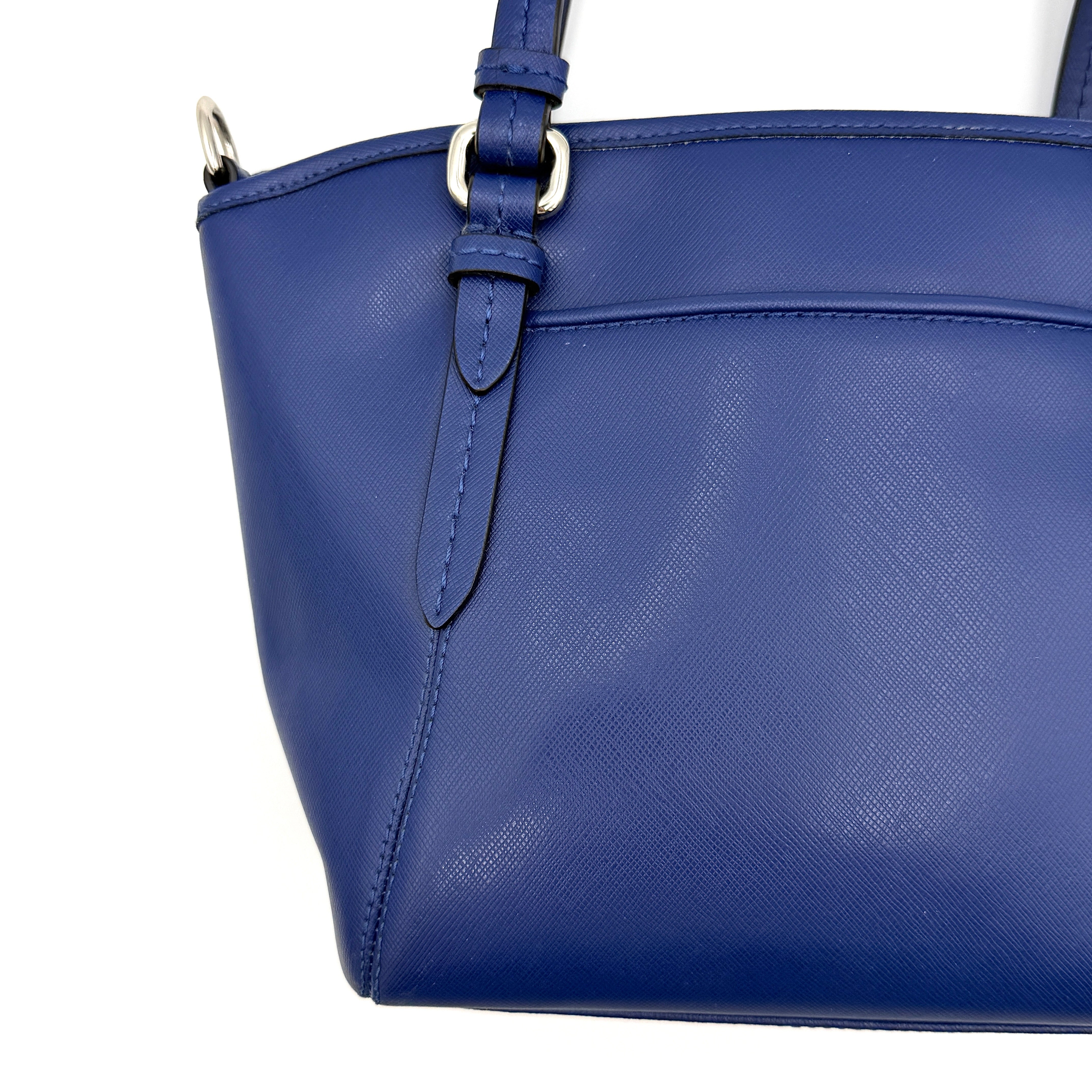 A structured cobalt blue Coach tote bag with silver hardware, dual handles, and an optional crossbody strap, displayed against a clean background.