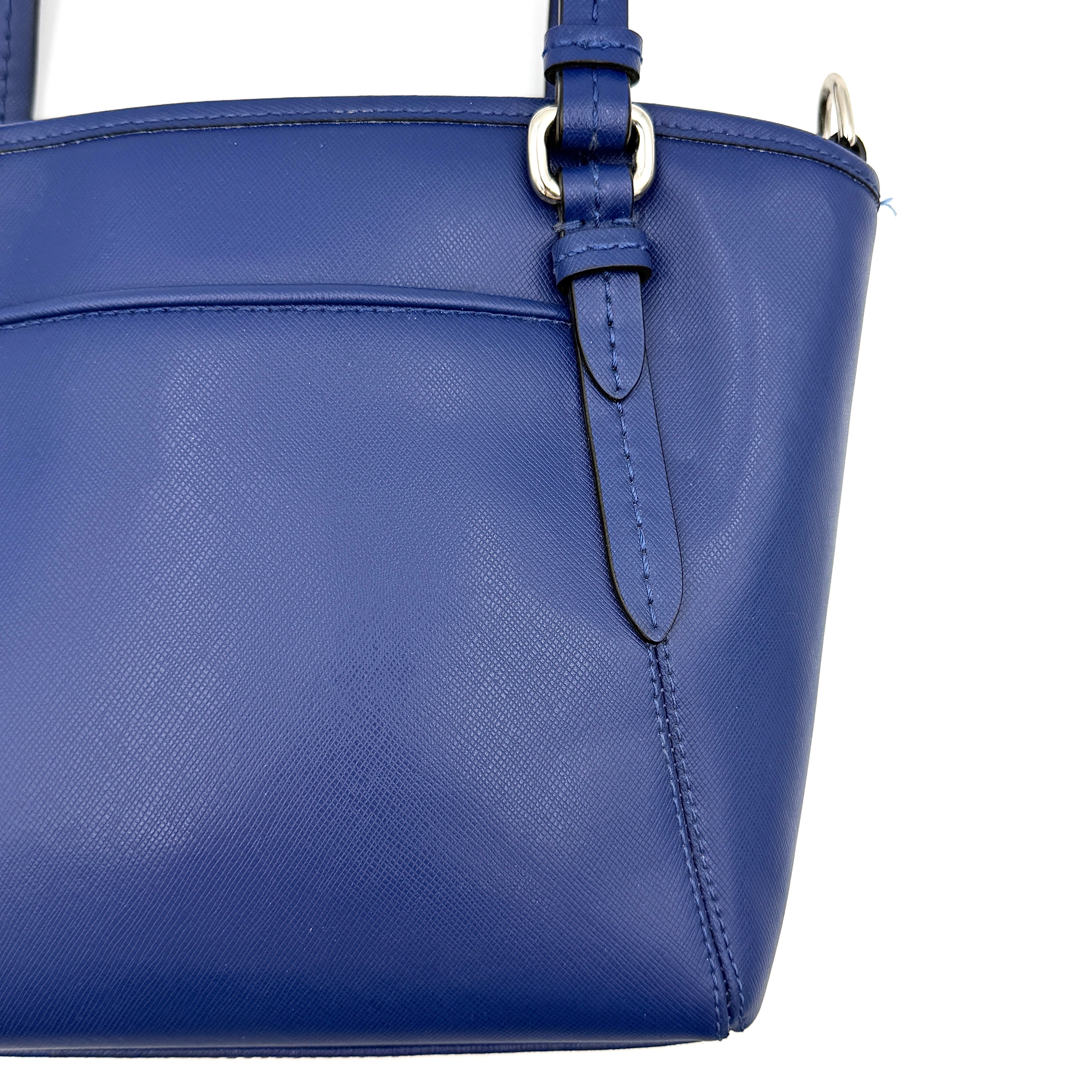 A structured cobalt blue Coach tote bag with silver hardware, dual handles, and an optional crossbody strap, displayed against a clean background.