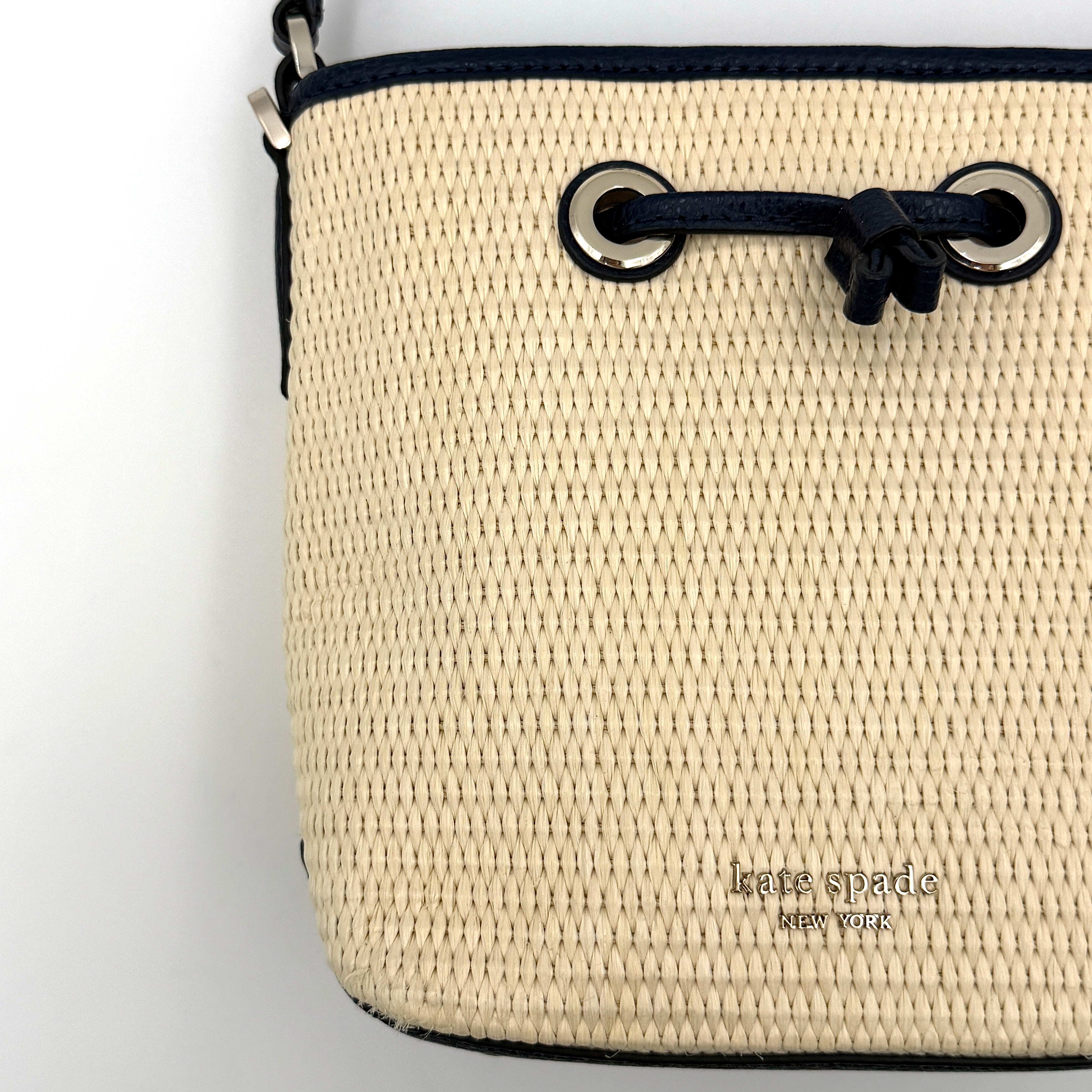 Front view of the Kate Spade Eva Straw Bucket Bag in cream, with navy leather trim and silver-tone hardware.