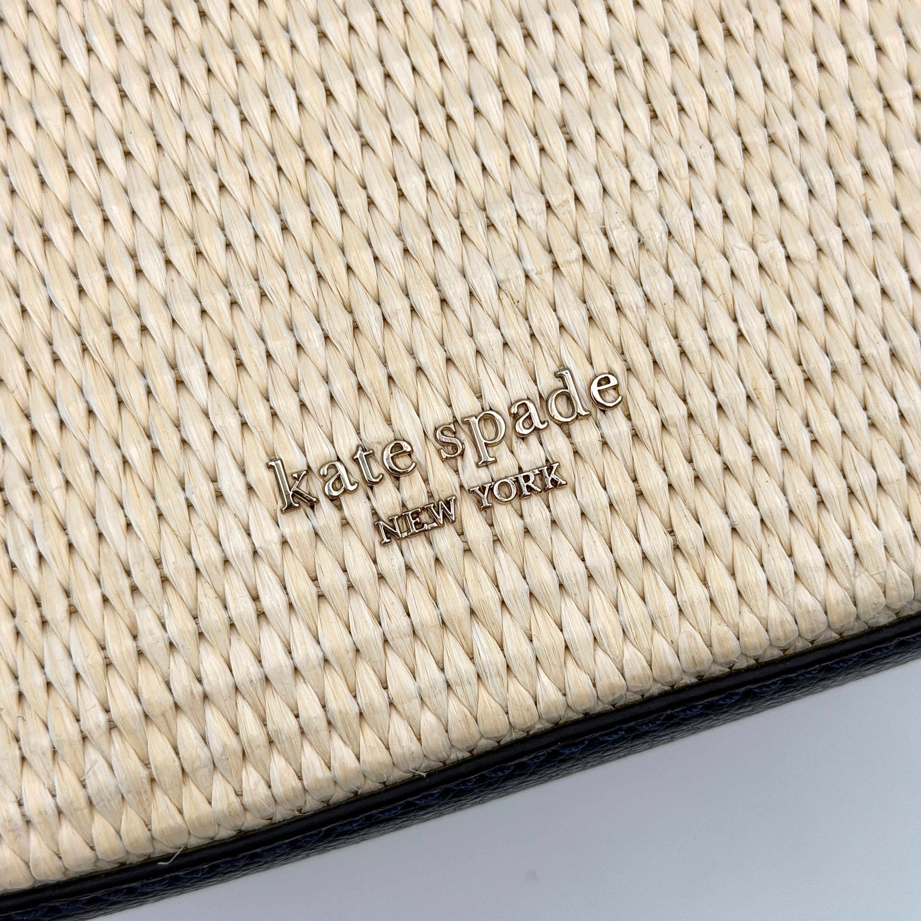 Front view of the Kate Spade Eva Straw Bucket Bag in cream, with navy leather trim and silver-tone hardware.
