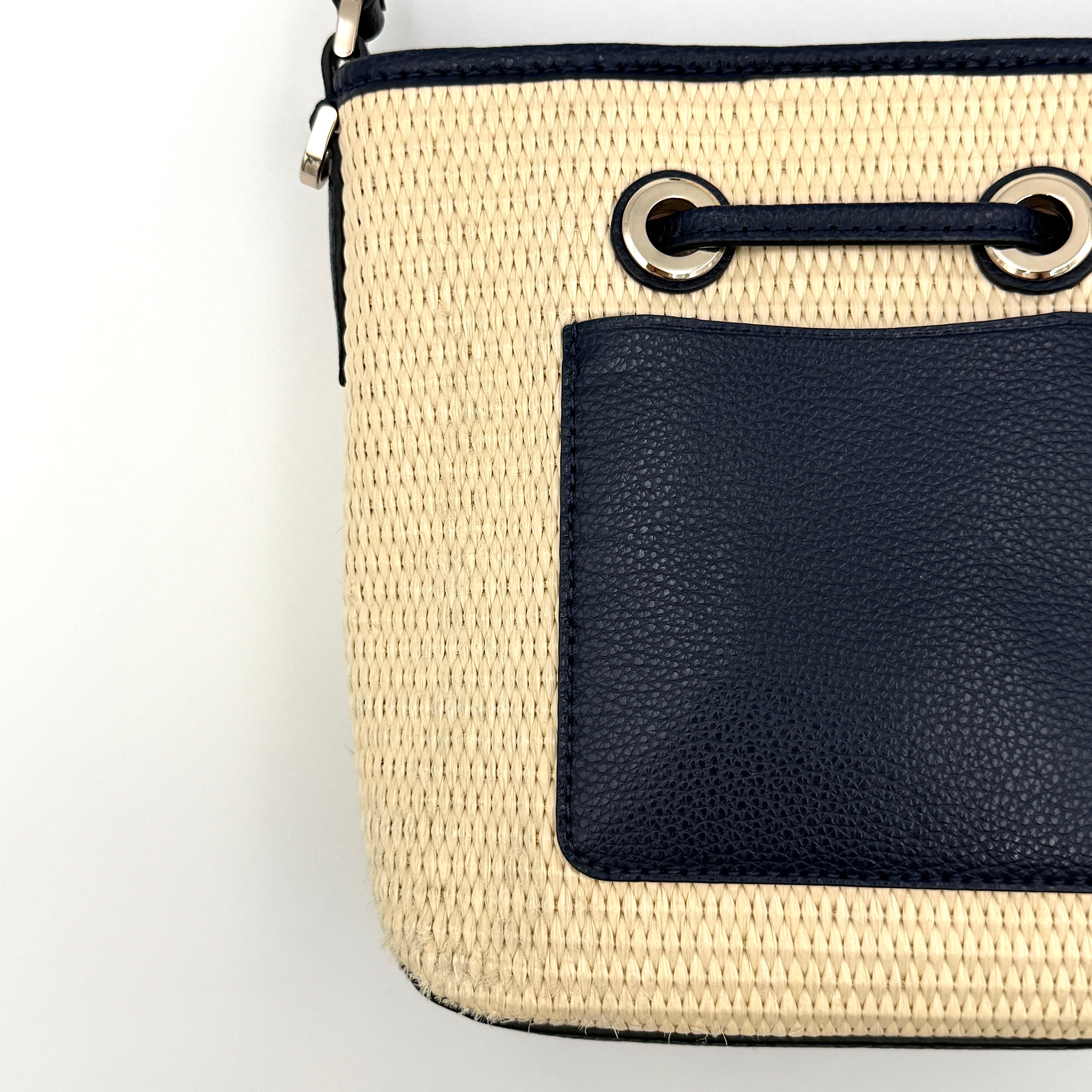 Front view of the Kate Spade Eva Straw Bucket Bag in cream, with navy leather trim and silver-tone hardware.