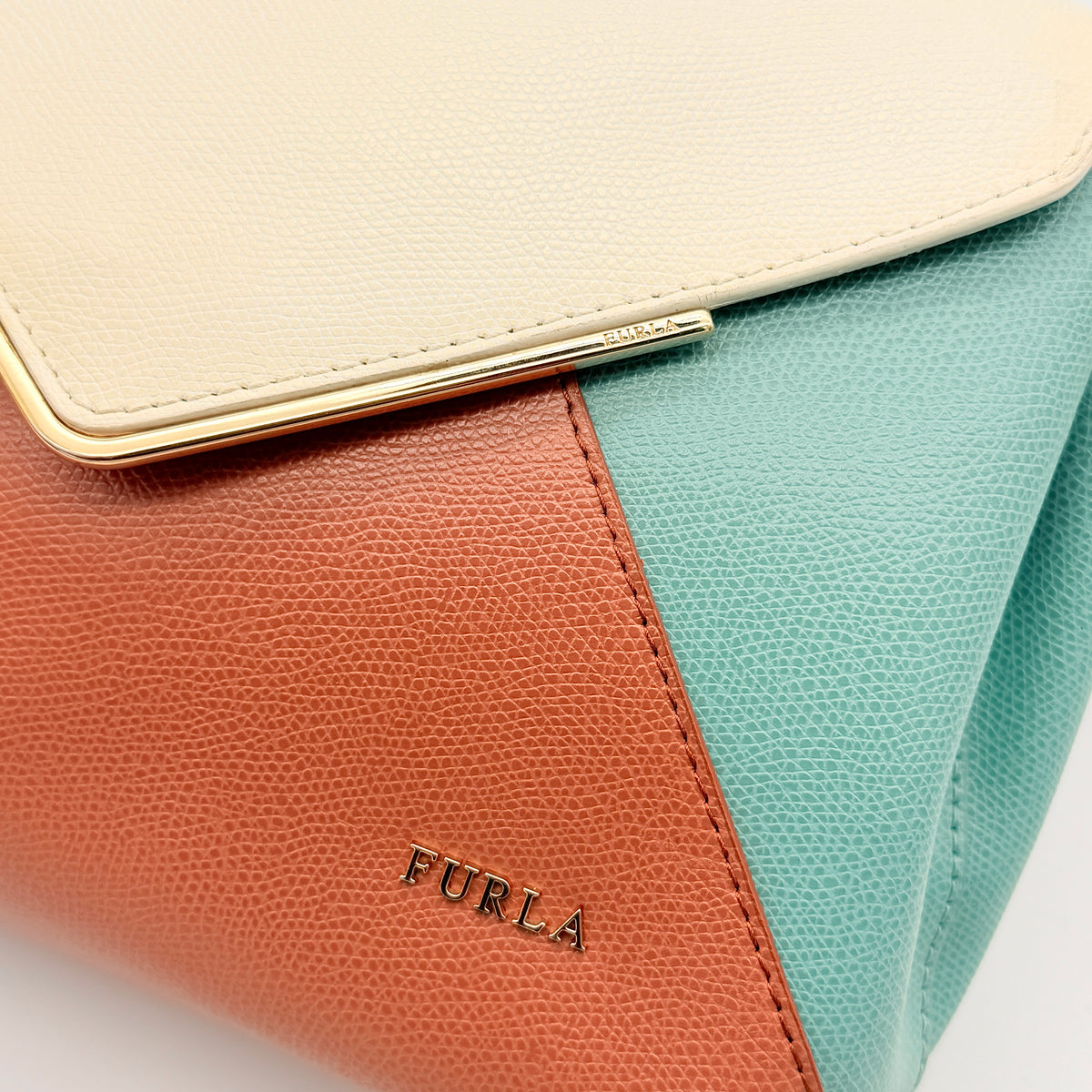 Furla Kelis crossbody bag in brown, blue, and cream leather with envelope flap and gold-tone hardware, displayed on a Furla dust bag.