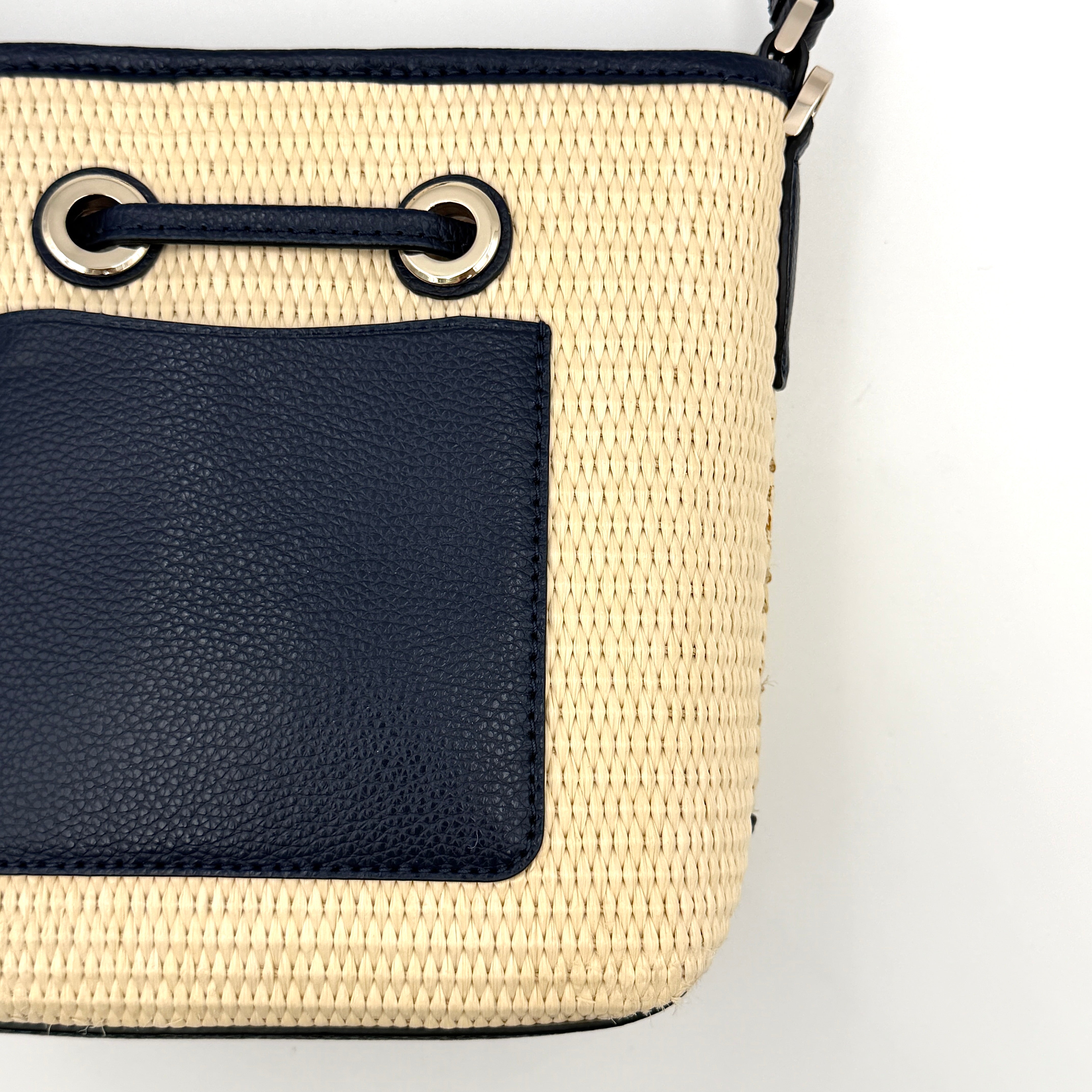 Front view of the Kate Spade Eva Straw Bucket Bag in cream, with navy leather trim and silver-tone hardware.