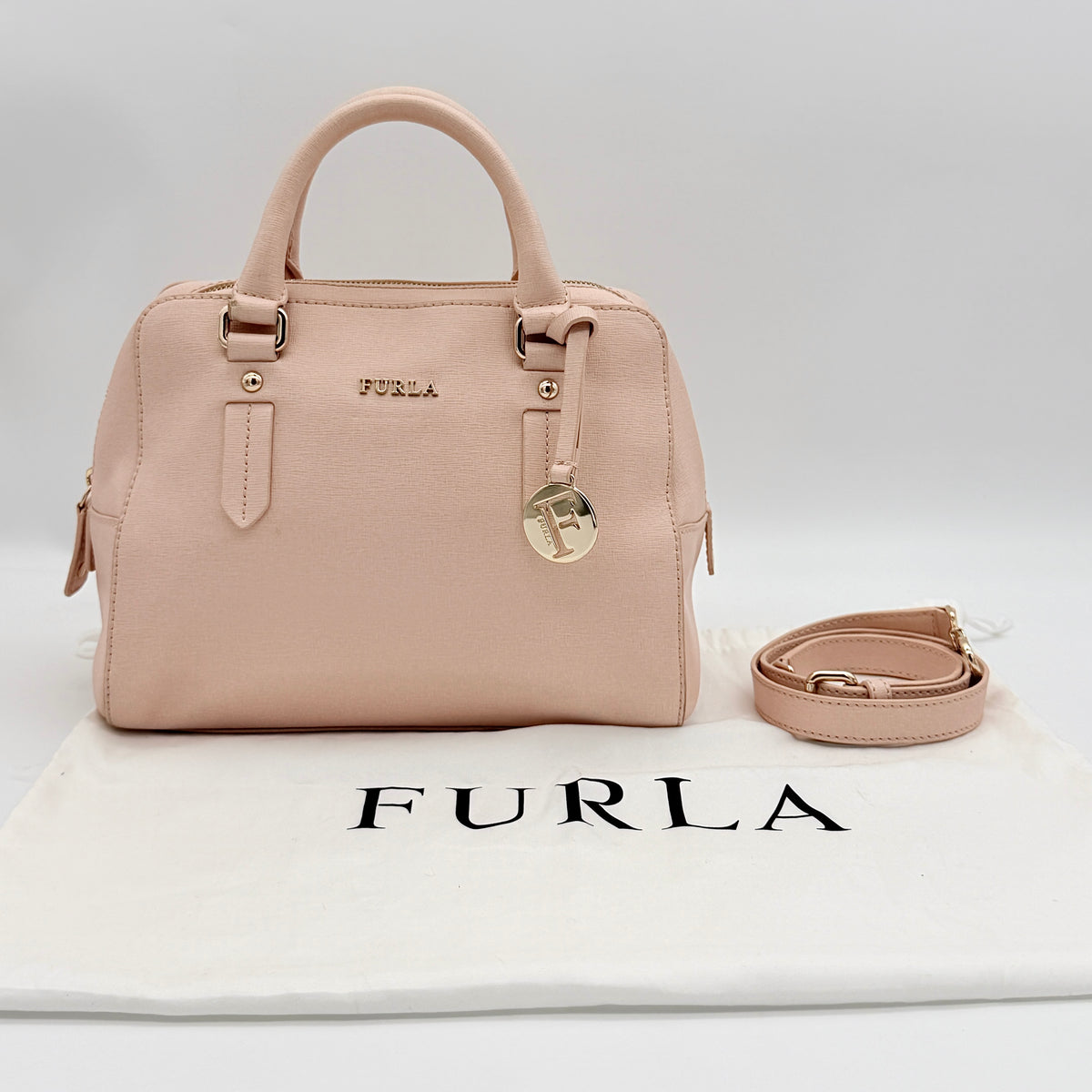 Furla Elena 2Way Saffiano leather satchel in beige with gold-tone hardware and removable strap, displayed on Furla-branded dust bag.