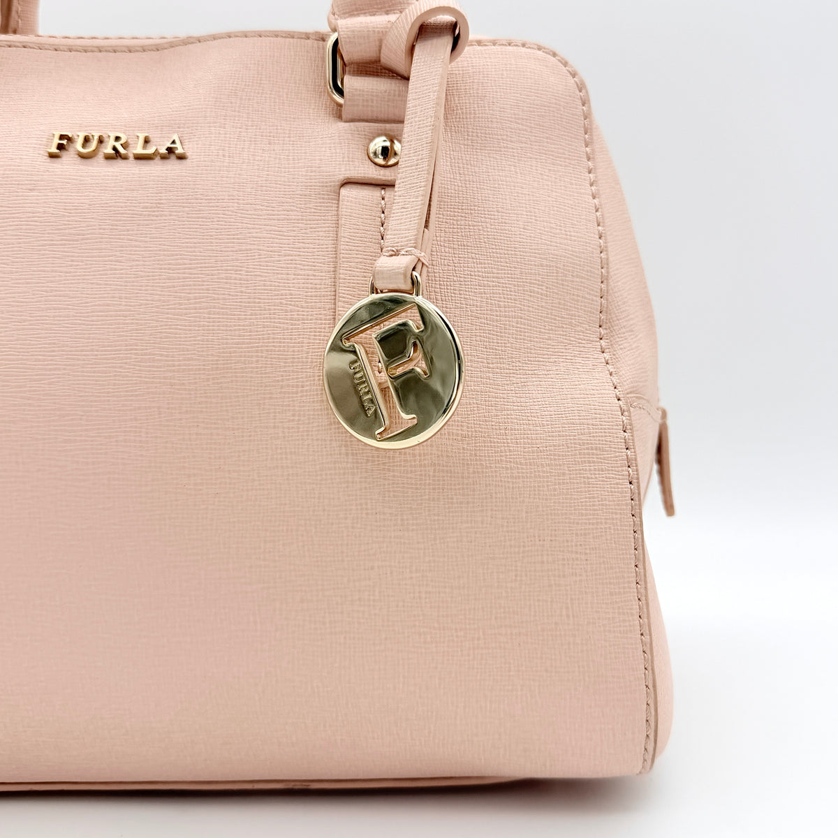 Furla Elena 2Way Saffiano leather satchel in beige with gold-tone hardware and removable strap, displayed on Furla-branded dust bag.