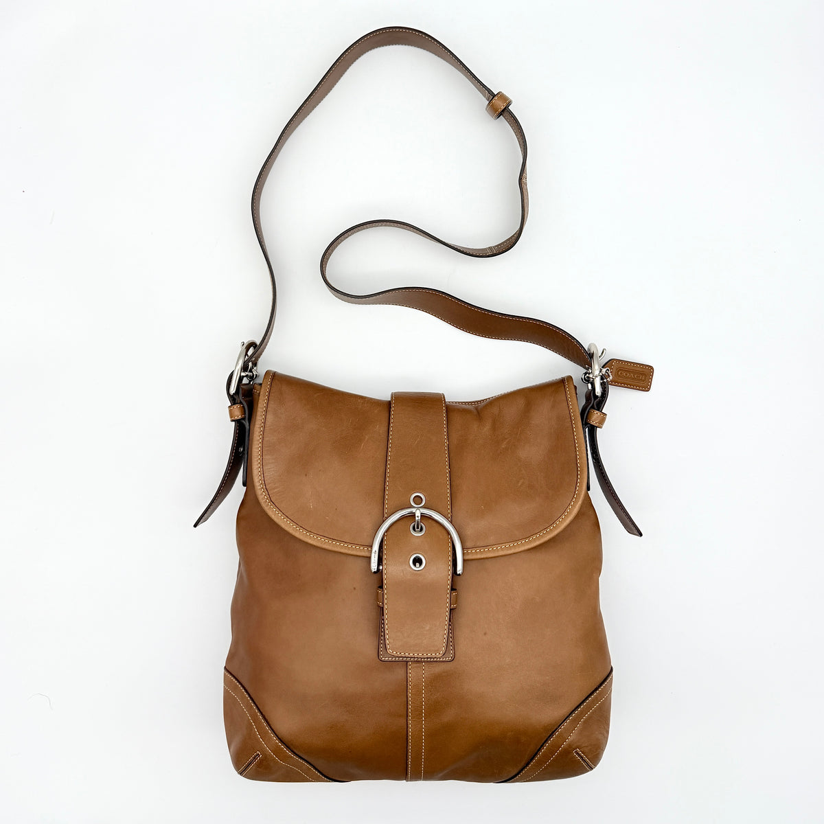 Coach Soho Buckle Flap Crossbody Bag in brown leather with buckle flap and adjustable strap, displayed on white background.
