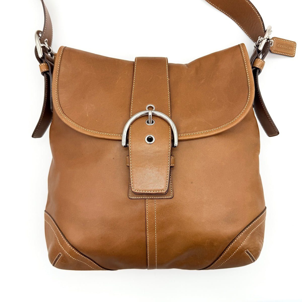Coach Soho Buckle Flap Crossbody Bag in brown leather with buckle flap and adjustable strap, displayed on white background.