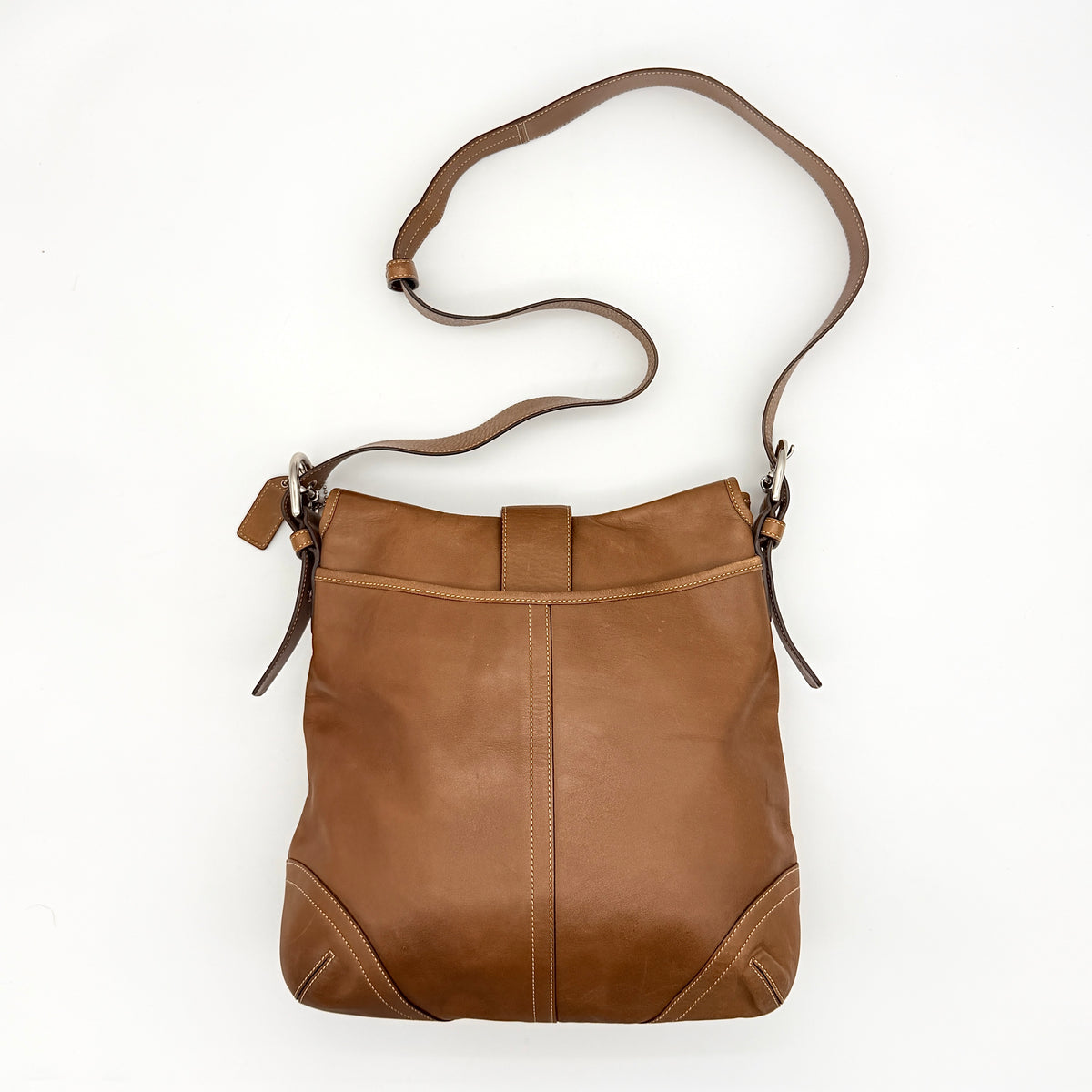Coach Soho Buckle Flap Crossbody Bag in brown leather with buckle flap and adjustable strap, displayed on white background.