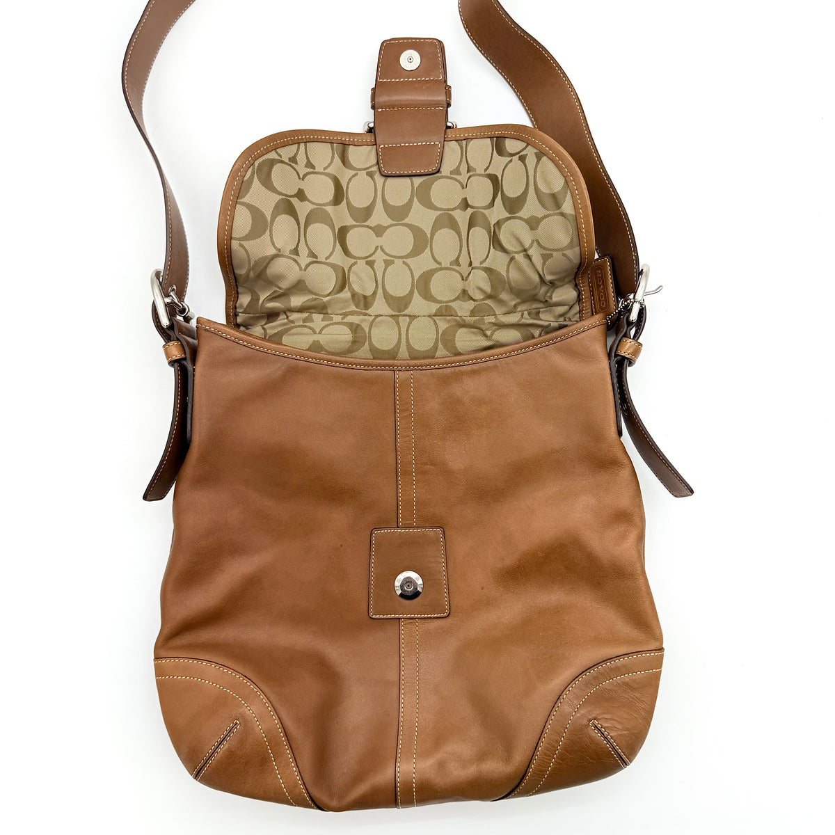 Coach Soho Buckle Flap Crossbody Bag in brown leather with buckle flap and adjustable strap, displayed on white background.