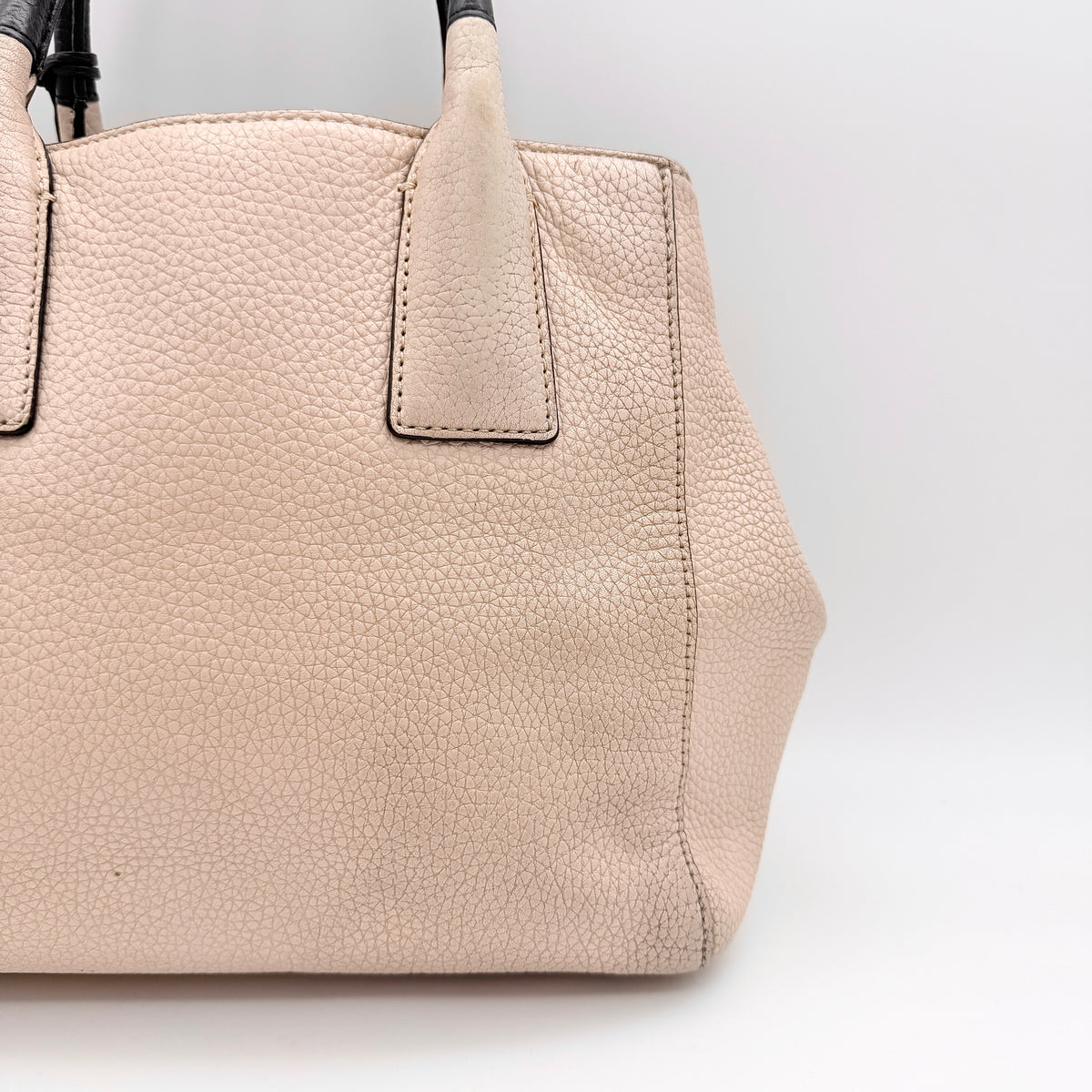 Kate Spade New York beige leather satchel with black handles, gold medallion, and grained texture against a white background.