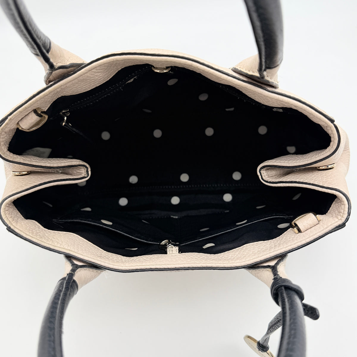 Kate Spade New York beige leather satchel with black handles, gold medallion, and grained texture against a white background.