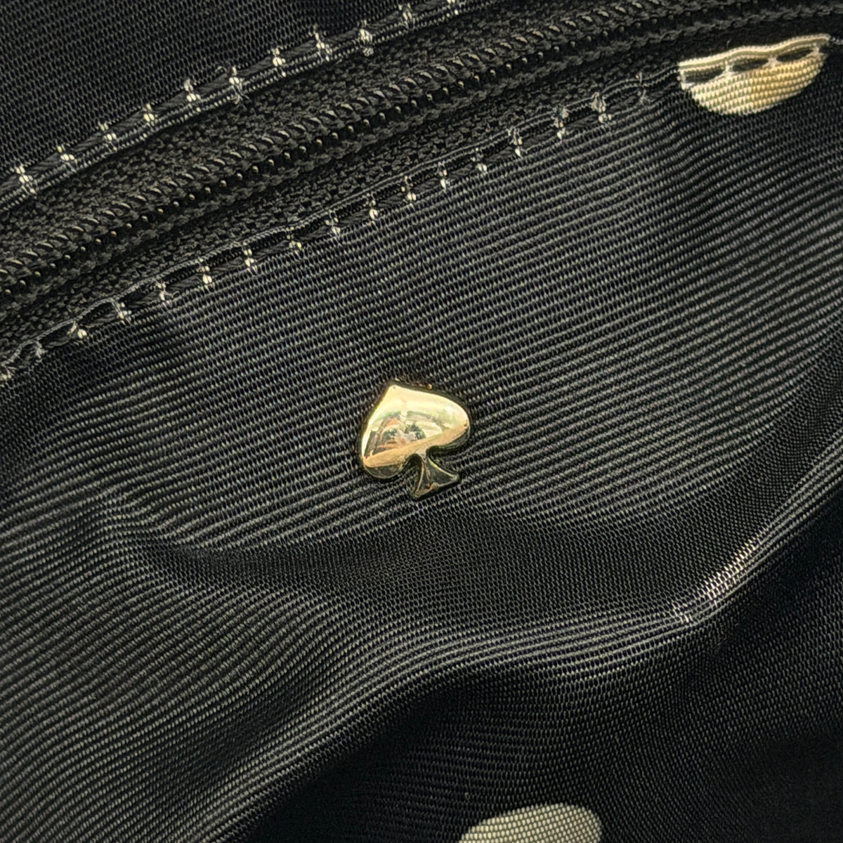 Kate Spade New York beige leather satchel with black handles, gold medallion, and grained texture against a white background.