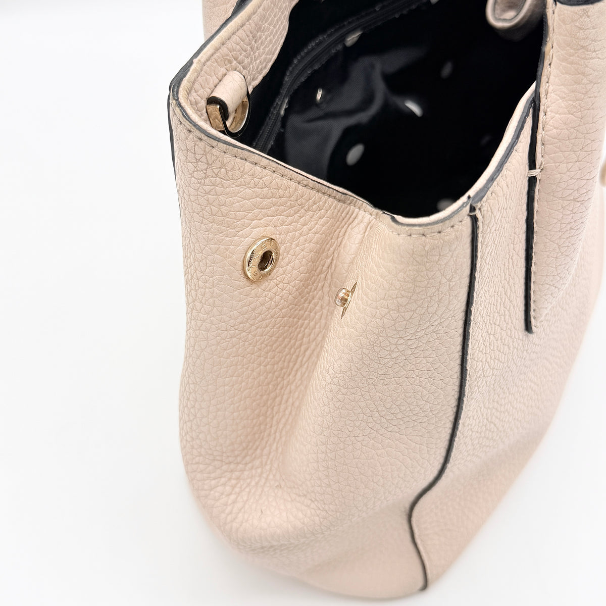 Kate Spade New York beige leather satchel with black handles, gold medallion, and grained texture against a white background.