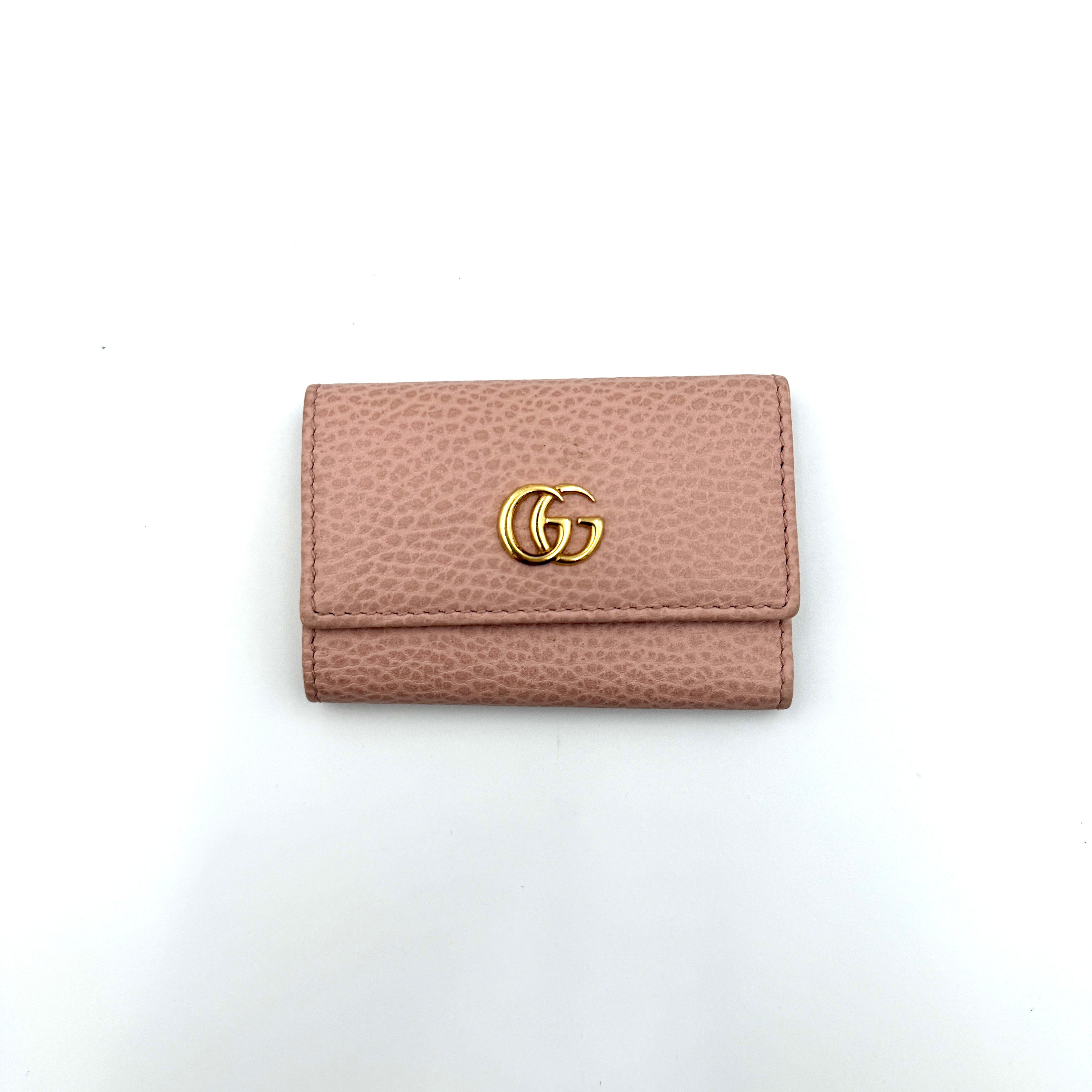 Gucci GG Marmont pink leather key case with gold GG emblem and grained texture, presented in a structured trifold shape.