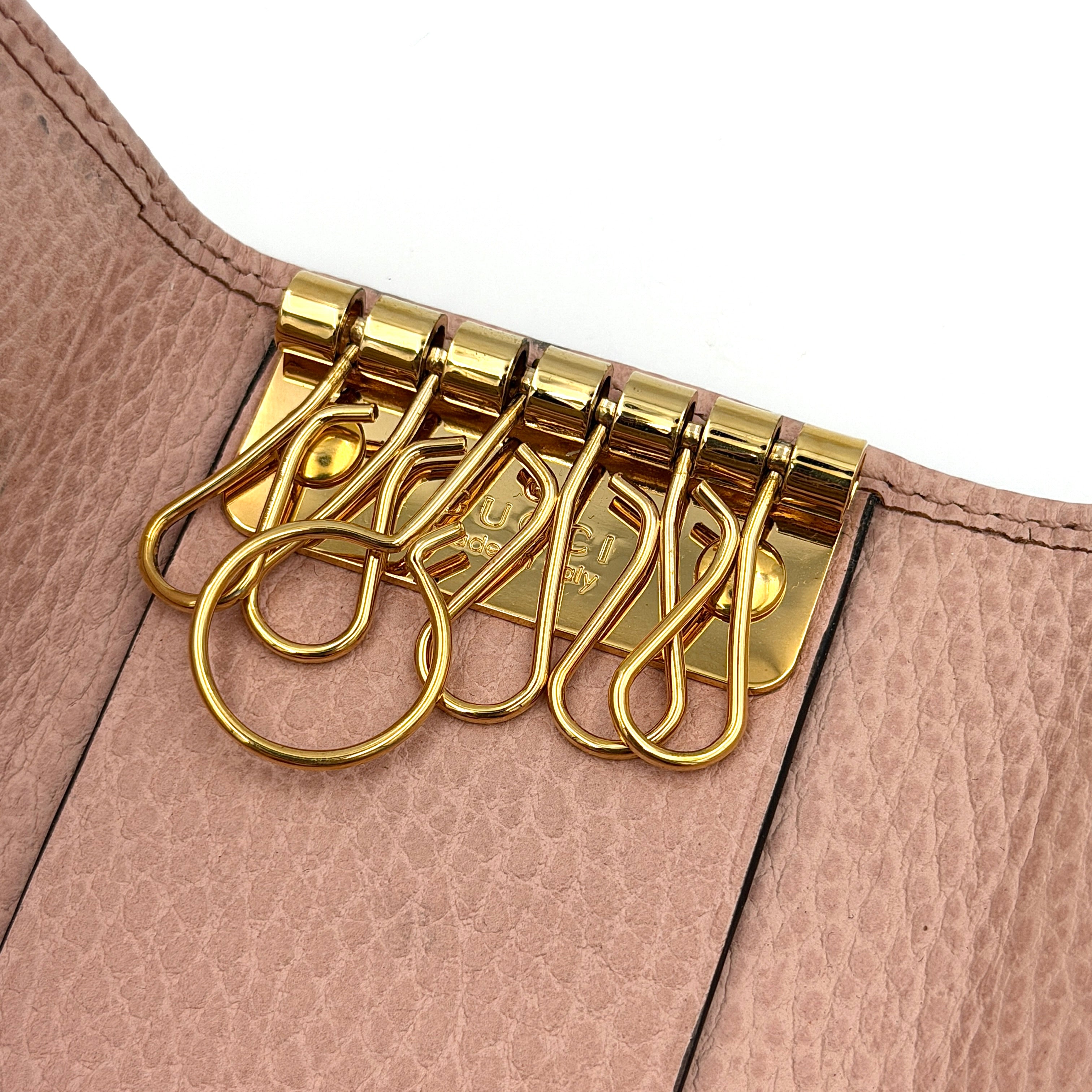 Gucci GG Marmont pink leather key case with gold GG emblem and grained texture, presented in a structured trifold shape.