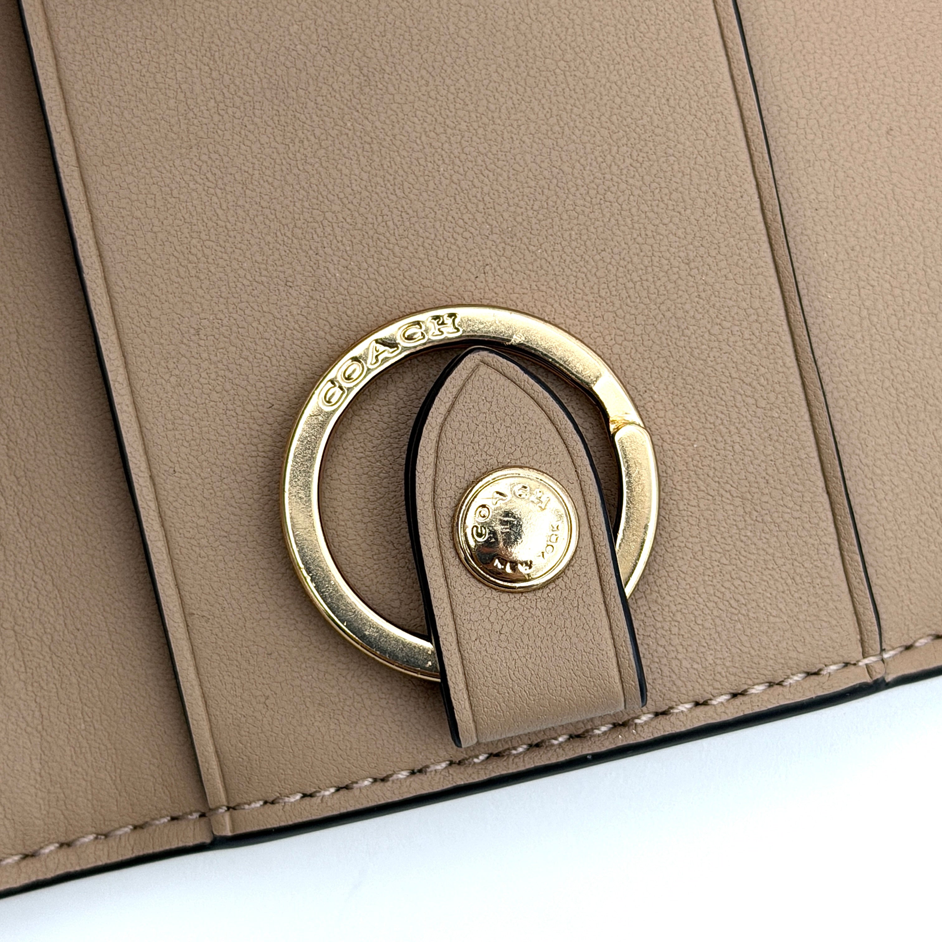 Coach floral print key case in cream with pink and brown blossom accents, gold hardware and structured silhouette.