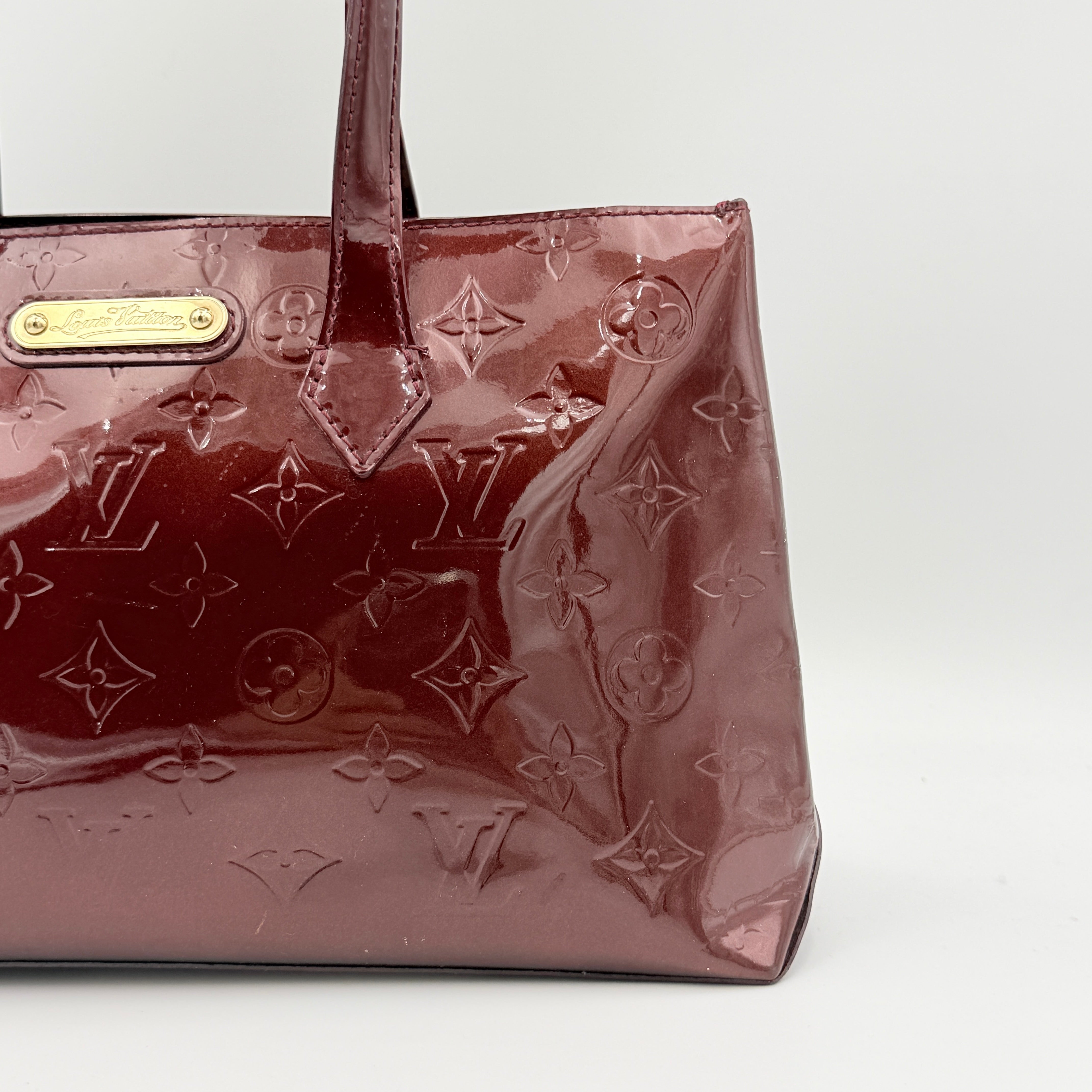 Louis Vuitton Wilshire PM Monogram Vernis bag in glossy deep red with gold nameplate and embossed monogram, displayed against a clean background.