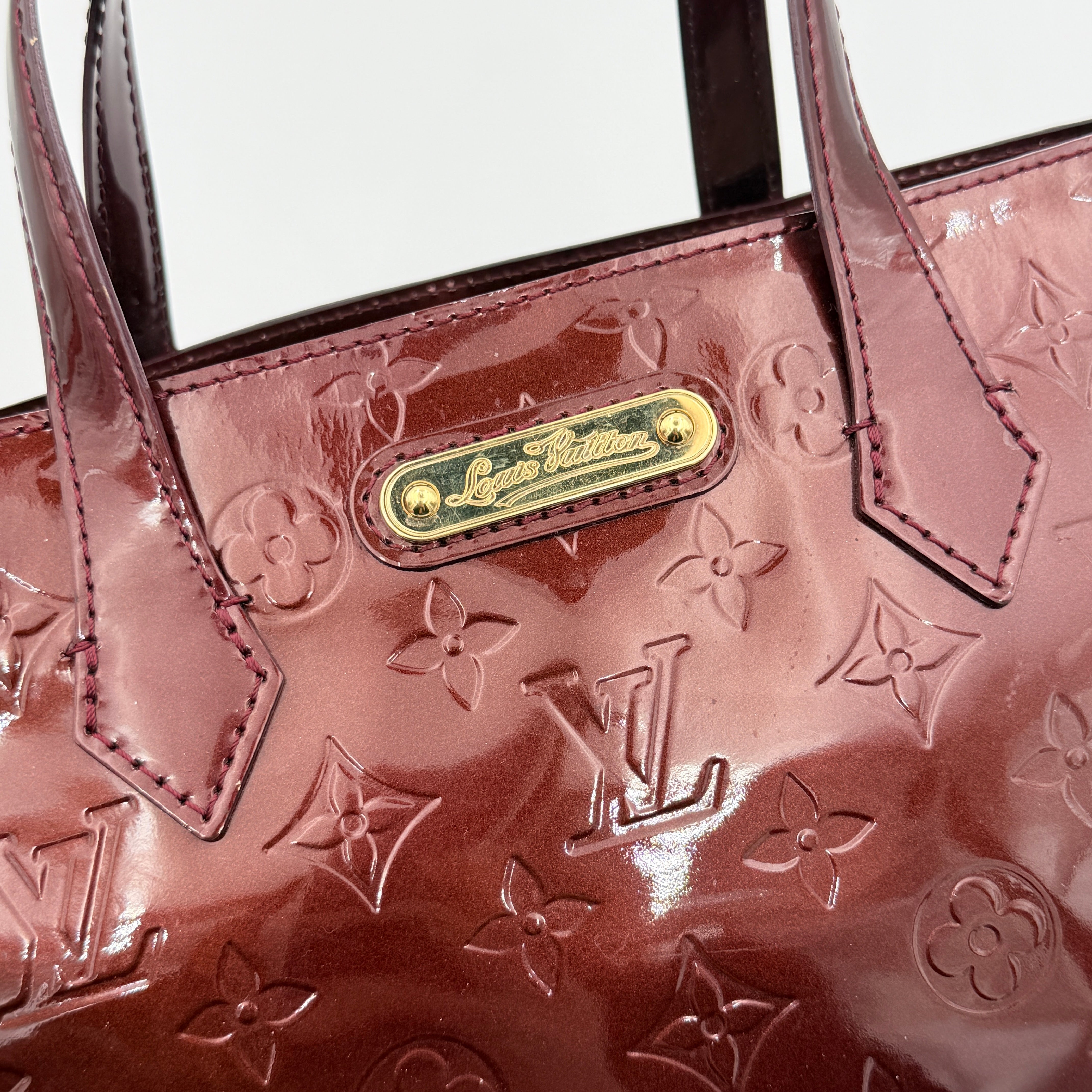 Louis Vuitton Wilshire PM Monogram Vernis bag in glossy deep red with gold nameplate and embossed monogram, displayed against a clean background.