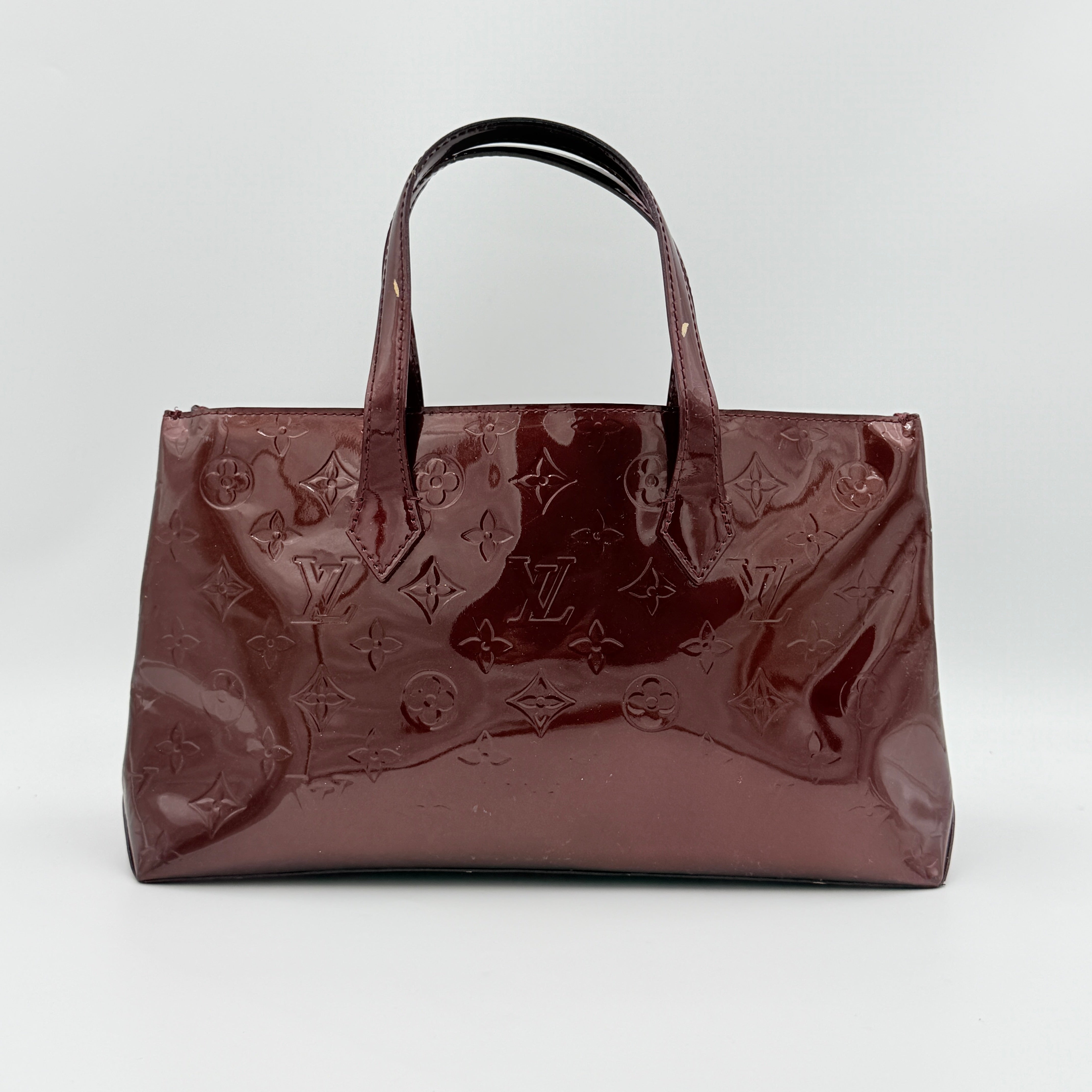 Louis Vuitton Wilshire PM Monogram Vernis bag in glossy deep red with gold nameplate and embossed monogram, displayed against a clean background.