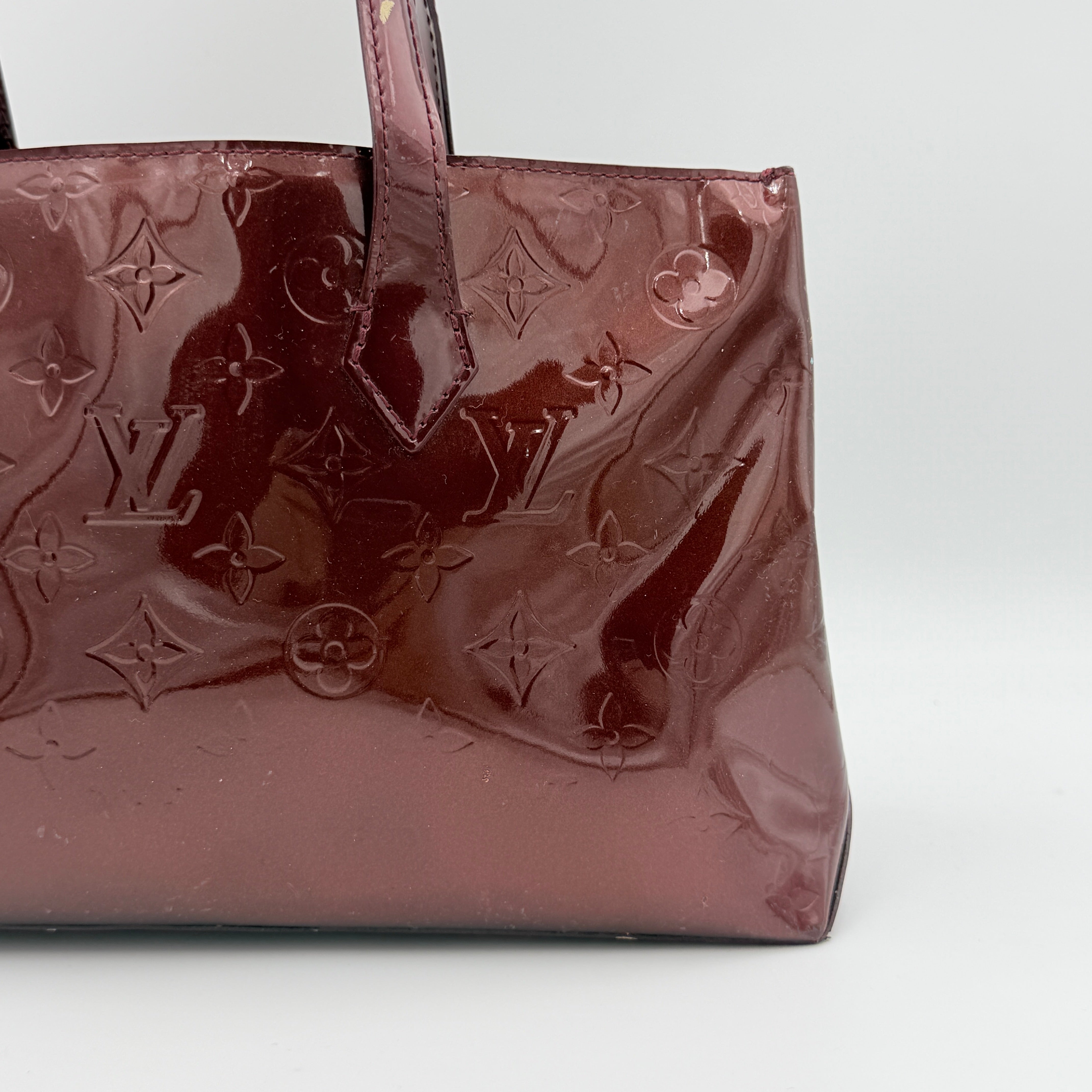 Louis Vuitton Wilshire PM Monogram Vernis bag in glossy deep red with gold nameplate and embossed monogram, displayed against a clean background.