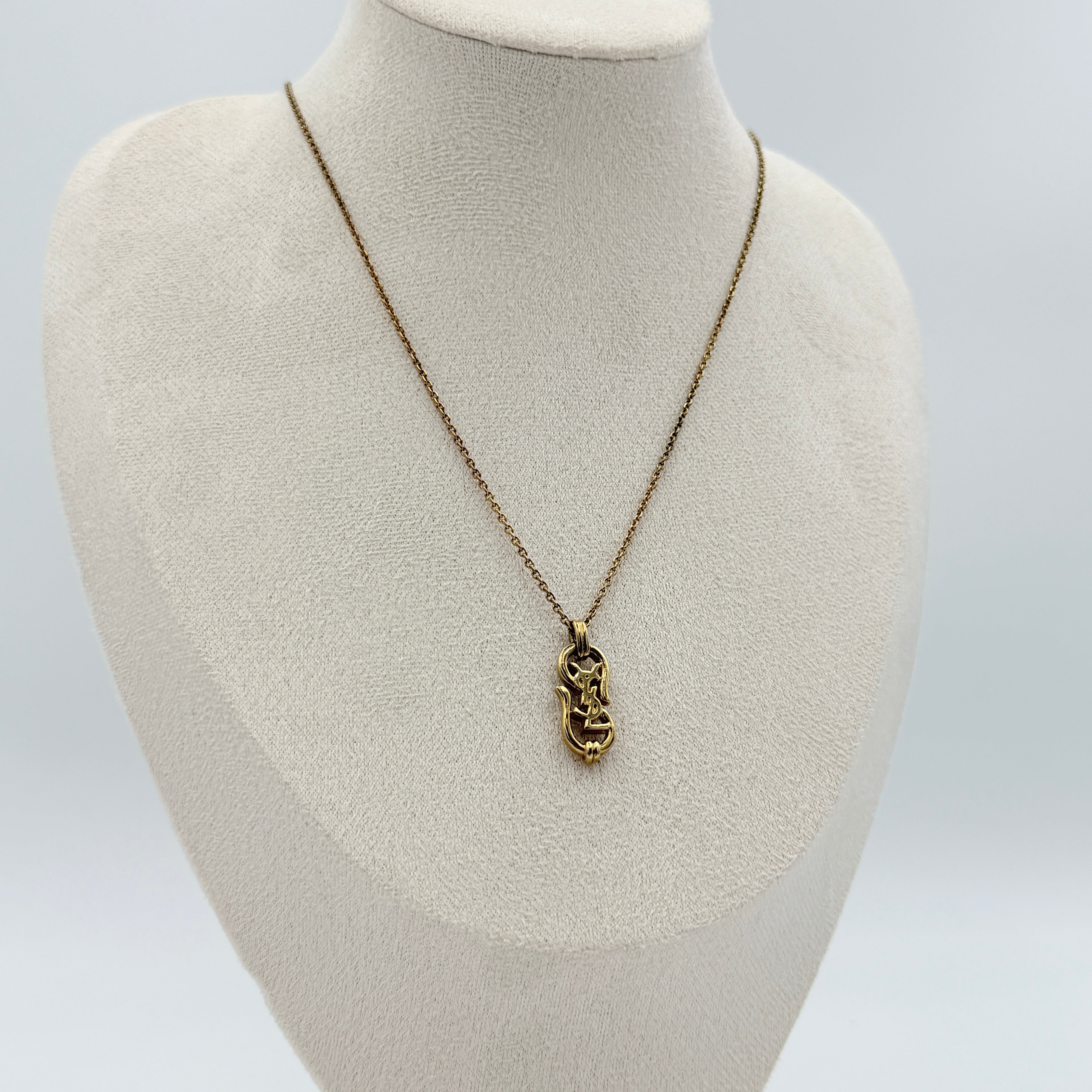 Saint Laurent Cassandre Logo Necklace in gold metal with signature YSL pendant displayed on a necklace stand.